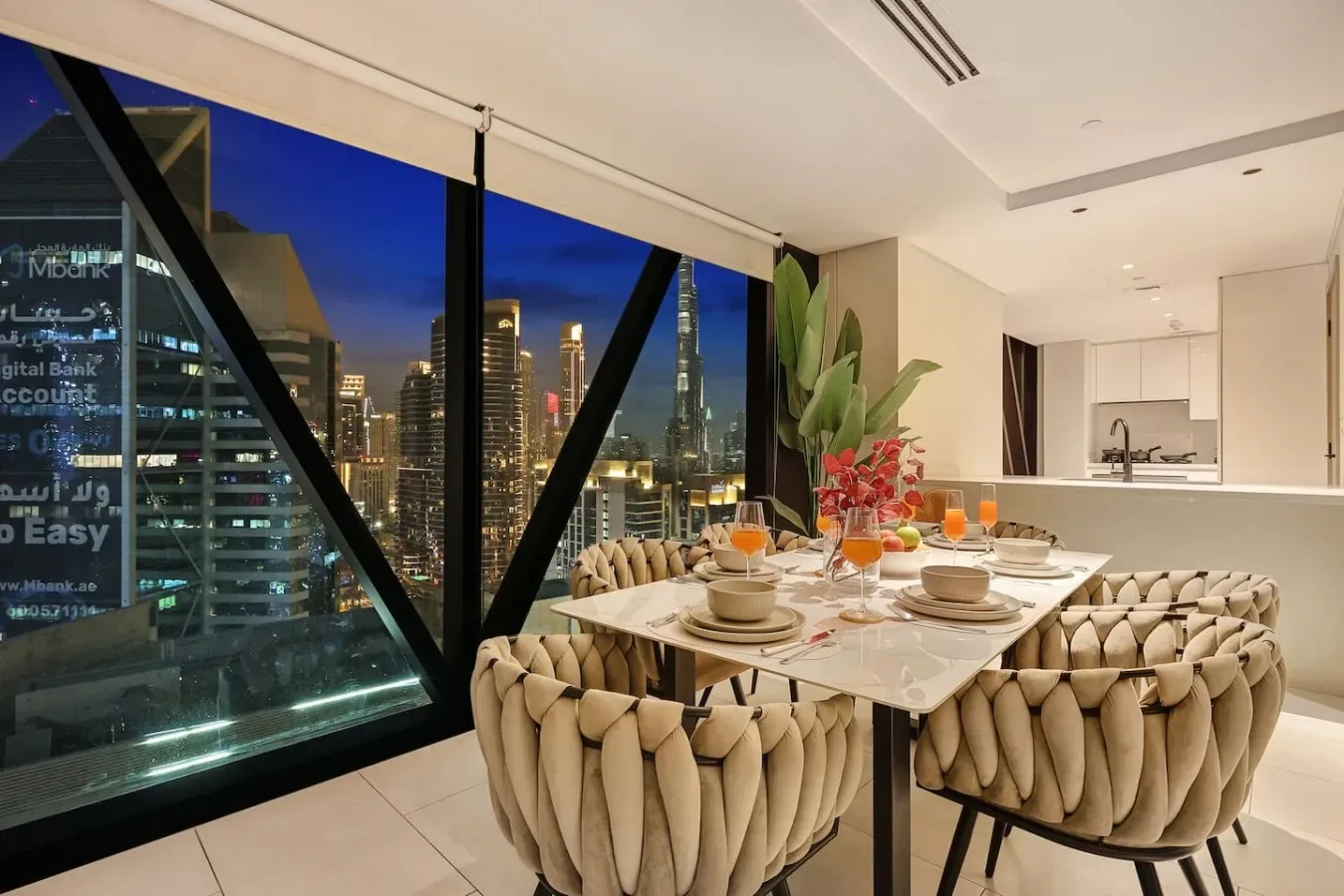 Un comedor con la mesa puesta y luces de la ciudad visibles por las grandes ventanas.