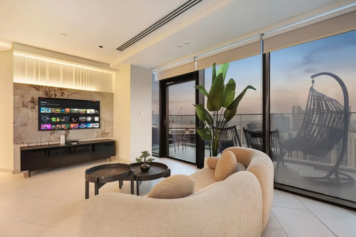 Una sala luminosa con asientos, un televisor y grandes ventanales que dan a un balcón.