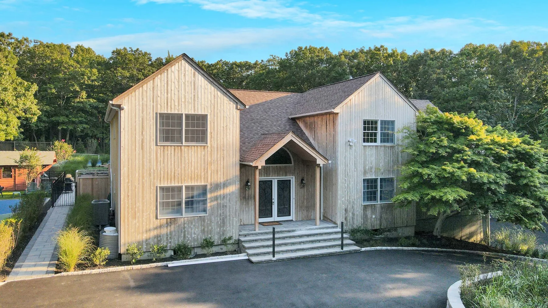 A two-story house with a covered entrance stands beside a paved driveway.