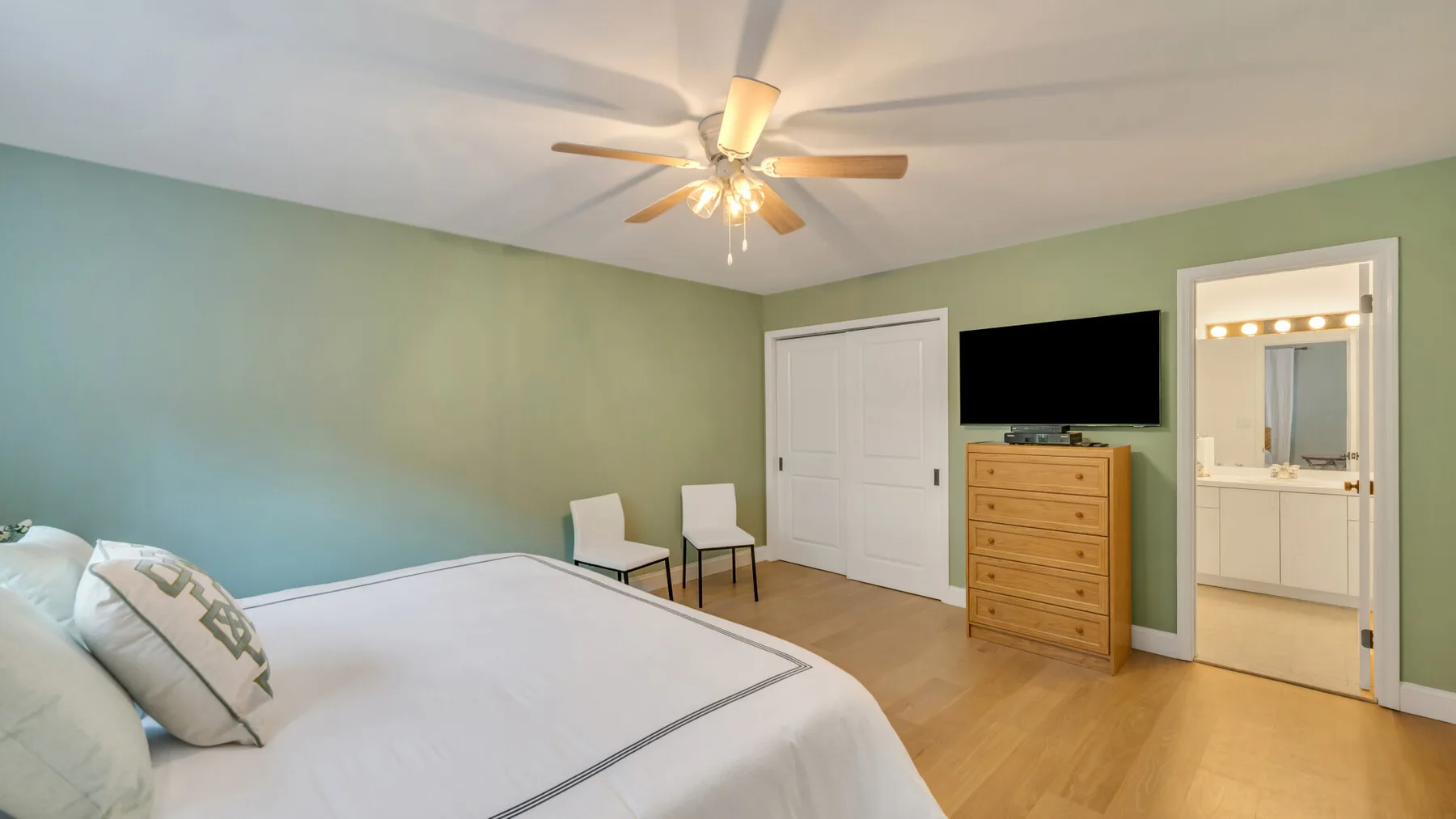 A bedroom with a bed, wooden dresser, and ceiling fan.