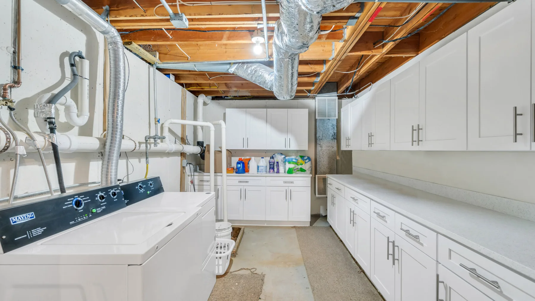 A laundry room with a washer and dryer beside white storage cabinets and a countertop.