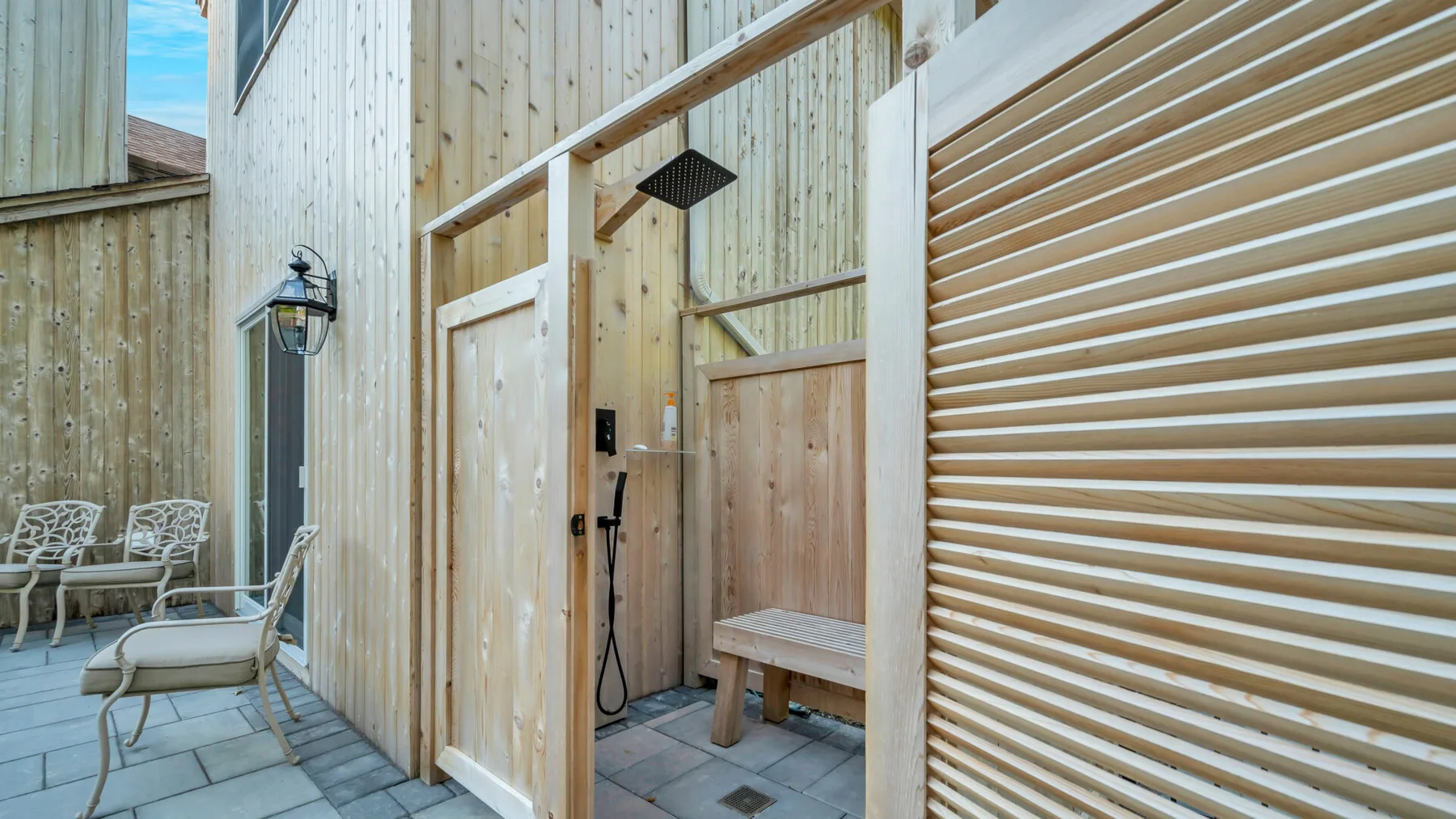 An outdoor shower area with a wooden bench beside light-colored wood siding.