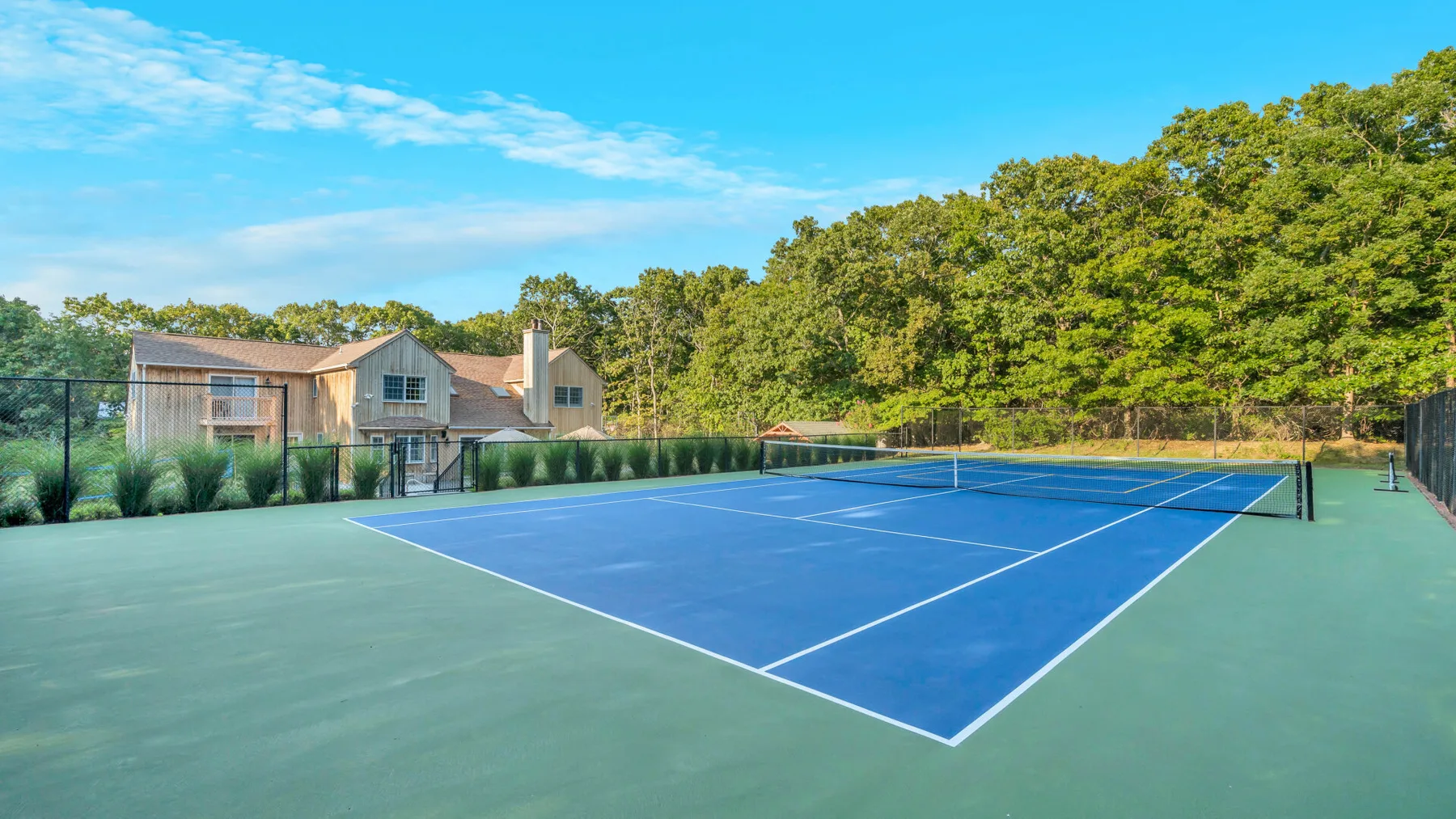 An outdoor tennis court bordered by fencing and trees.