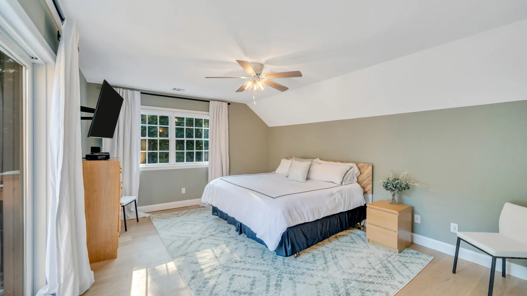 A bright bedroom with a large bed, windows, and a ceiling fan.
