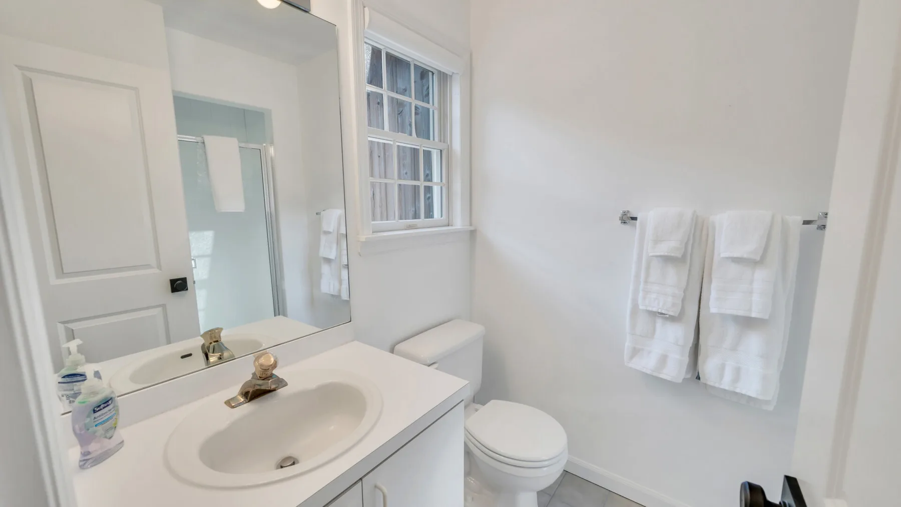 A bright bathroom with a sink, toilet, and towels hanging on the wall.
