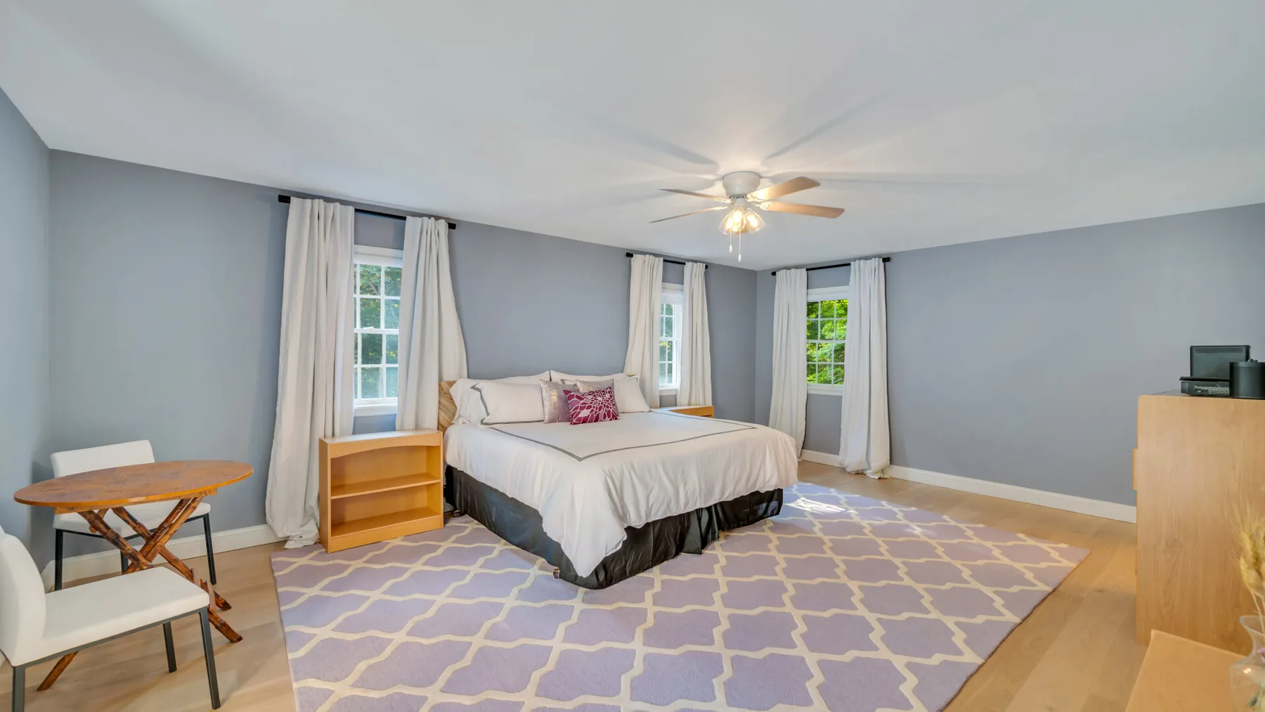 A bedroom with a bed, pale walls, and a patterned rug.