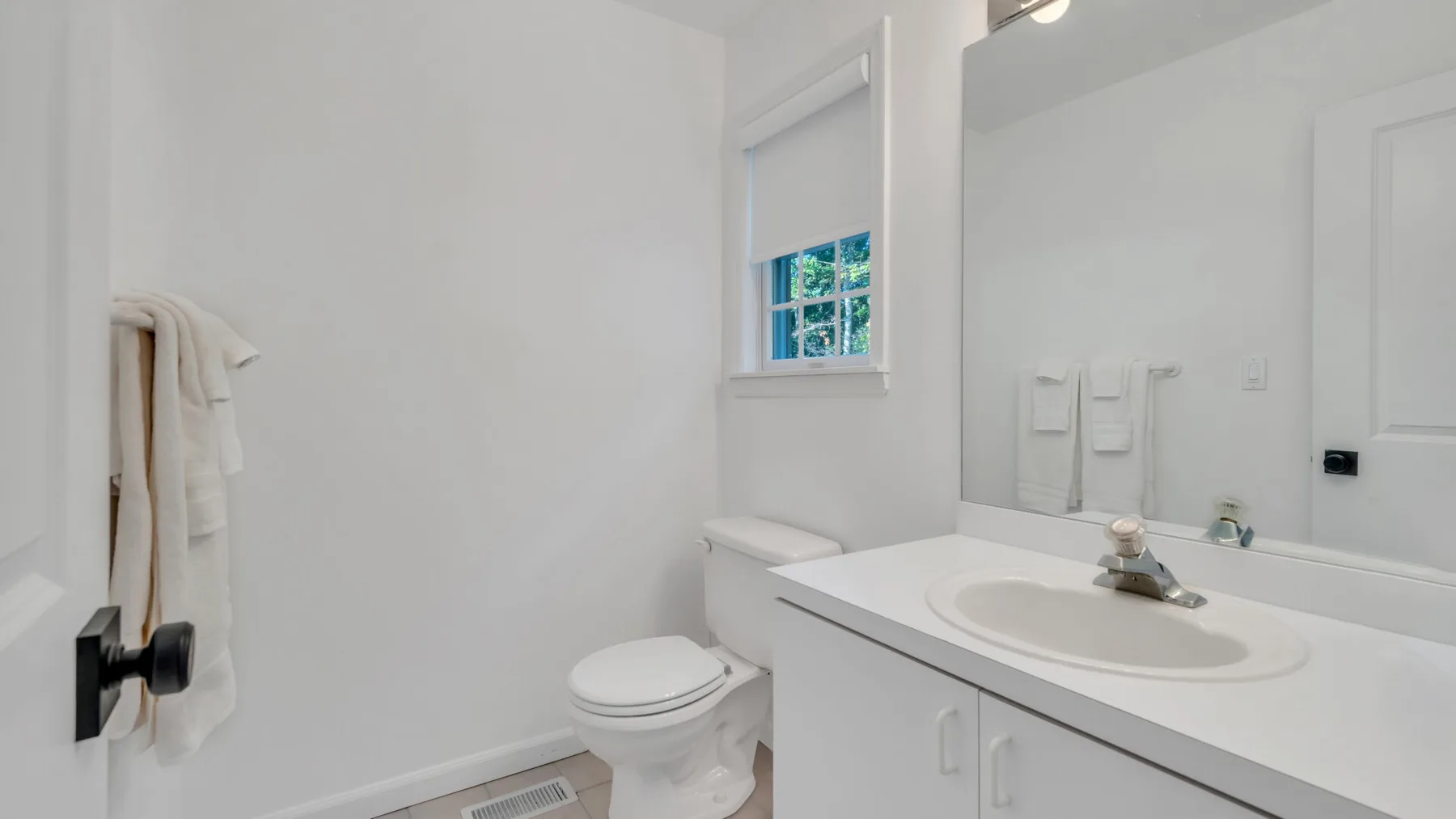 A bright bathroom with a sink, mirror, and toilet.