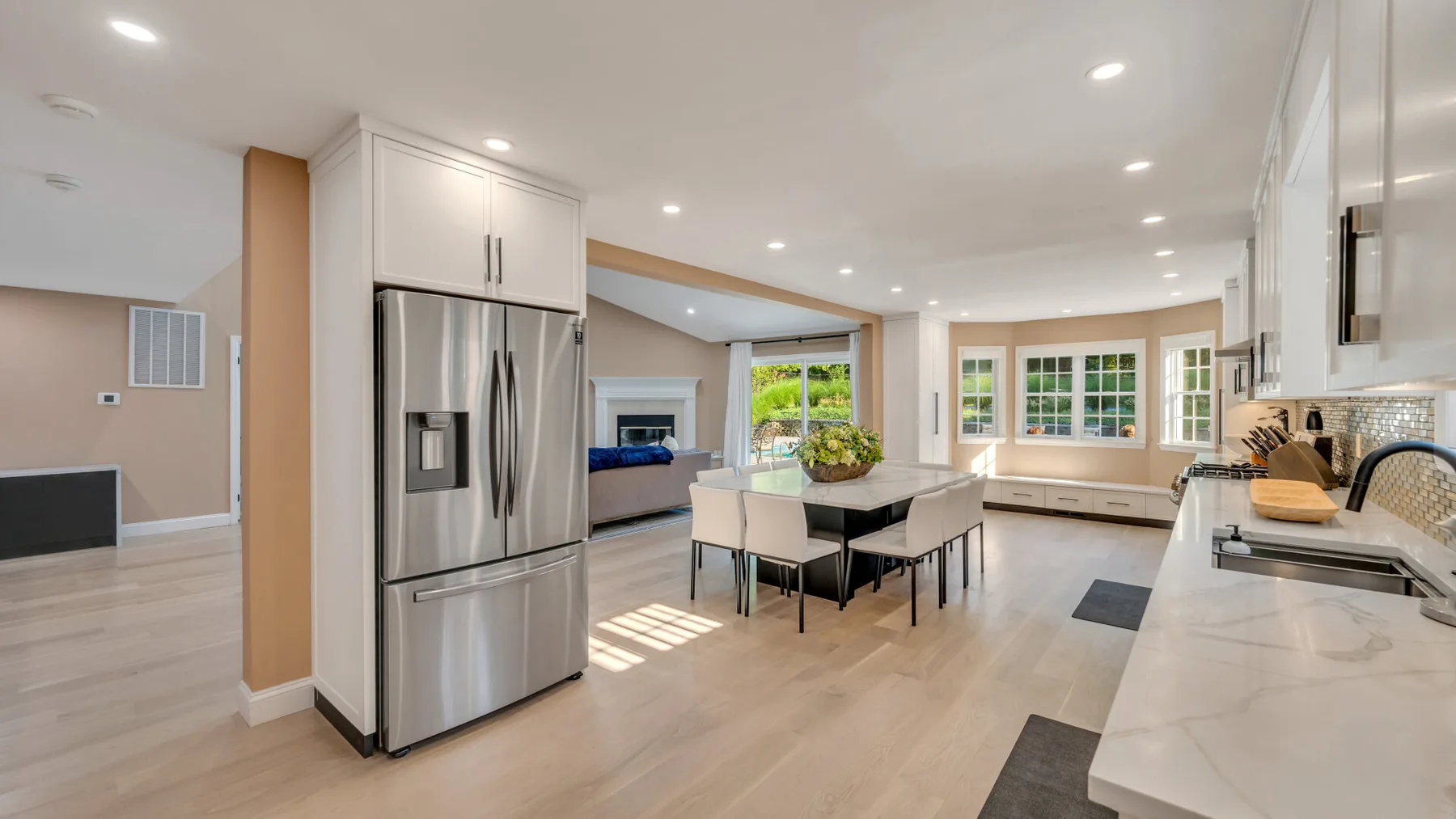 A bright open-plan kitchen and dining area with a large island and stainless-steel refrigerator.