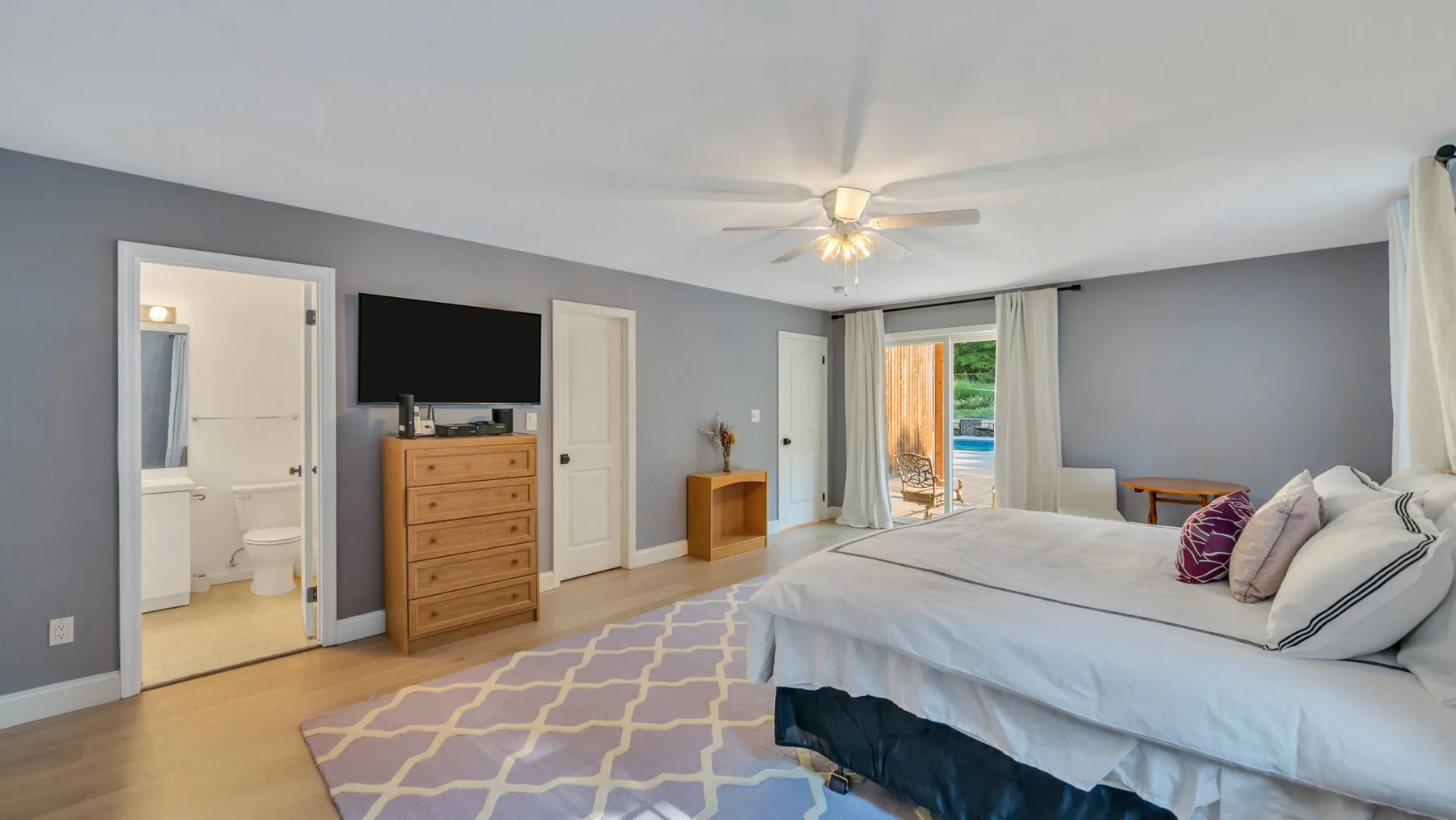 A bedroom with a large bed, a dresser, and a sliding glass door.