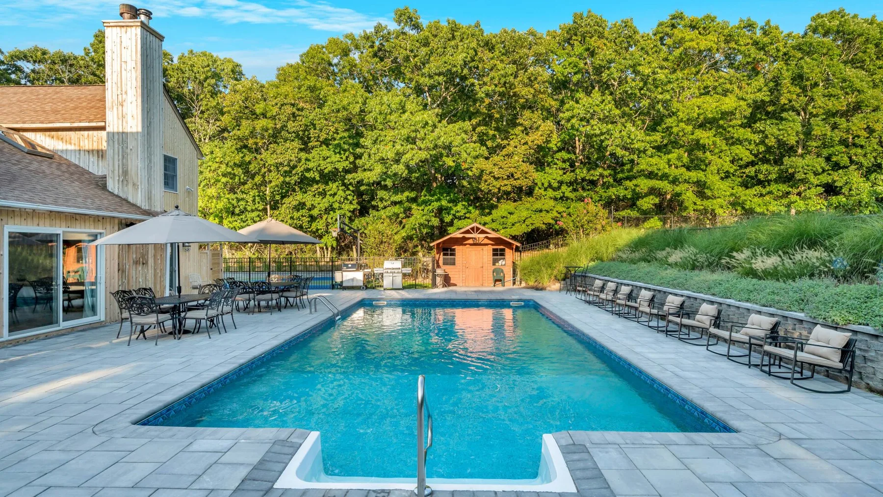 An outdoor swimming pool with lounge seating and a wooded backdrop.