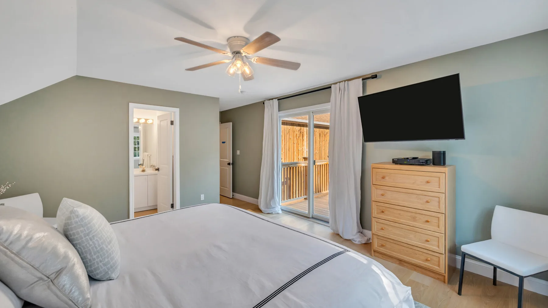 A bedroom with a large bed, ceiling fan, and sliding glass doors.