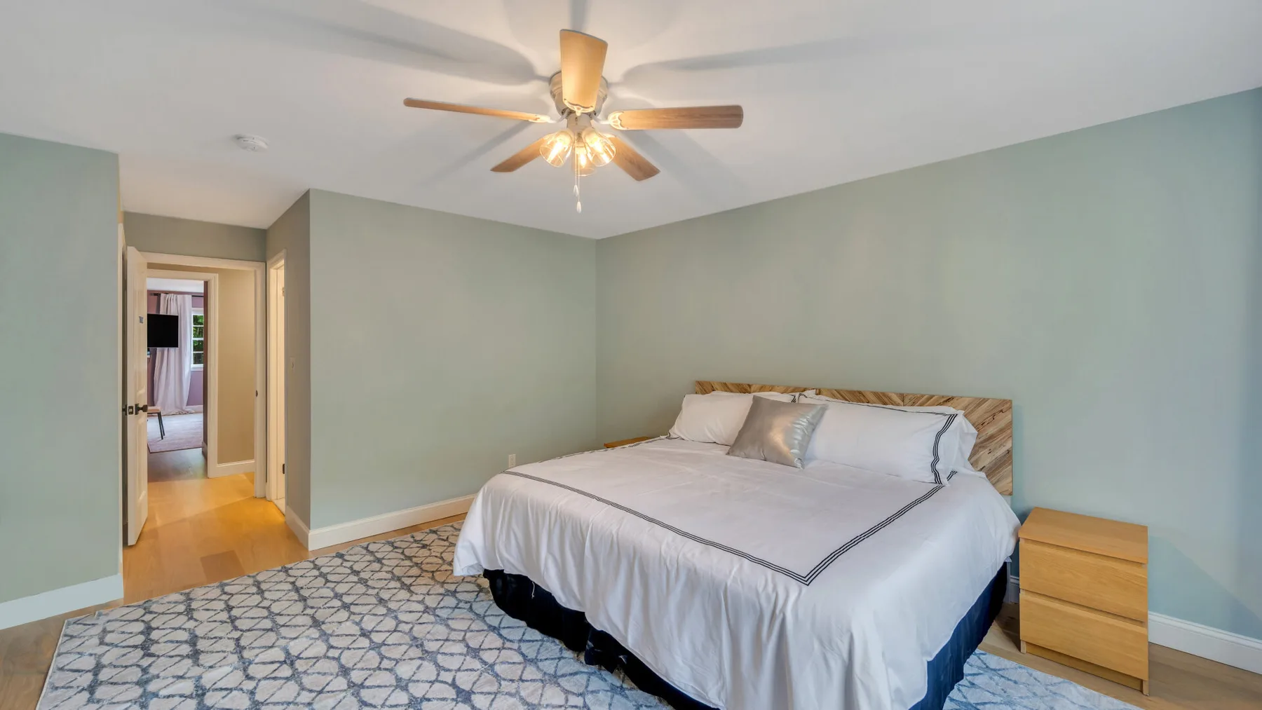 A bedroom with a bed, patterned rug, and ceiling fan.