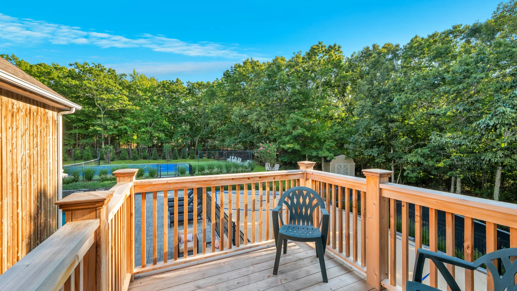 A wooden deck overlooks a swimming pool and a wooded area.