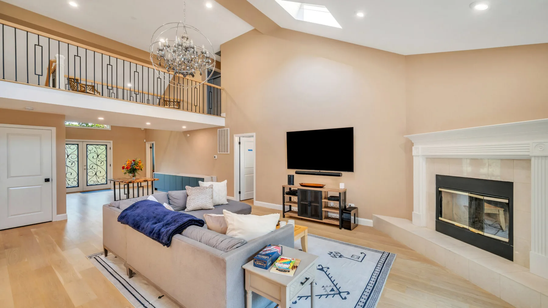 A bright living room with a seating area, television, and fireplace beneath a high ceiling.