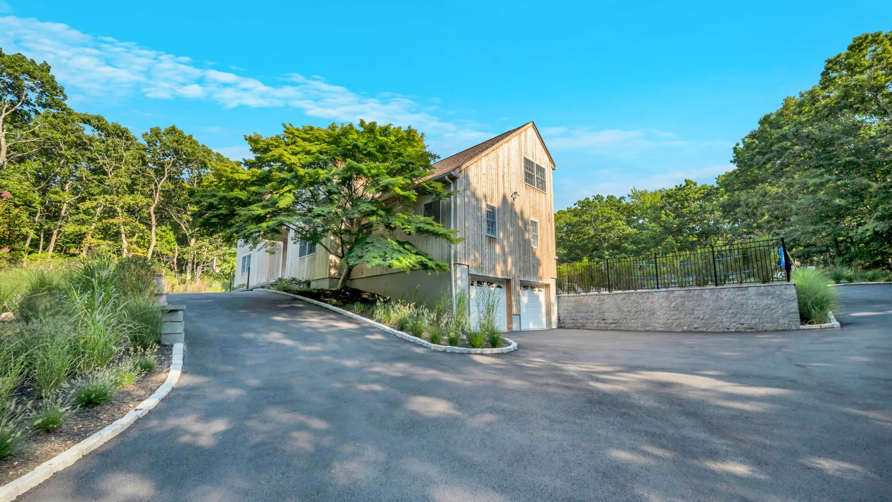 A modern wood-clad building stands beside a paved driveway and landscaped greenery.