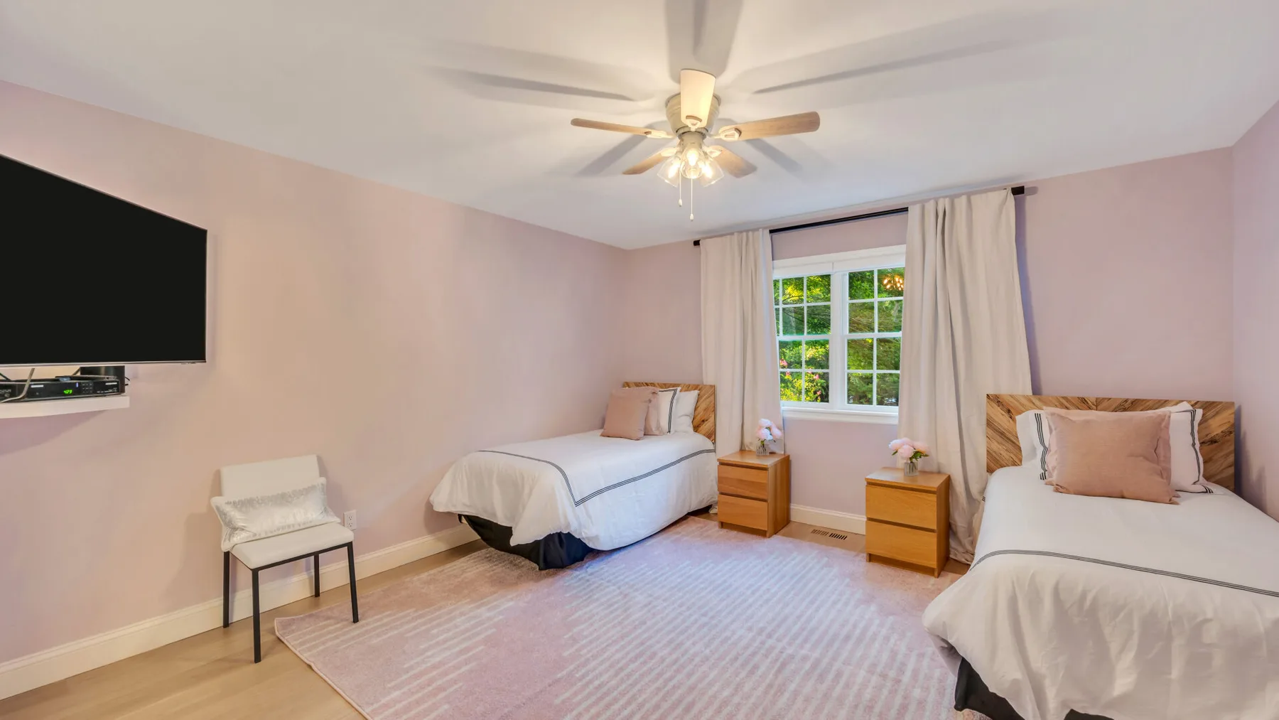 A bedroom with two beds, a window, and a ceiling fan.