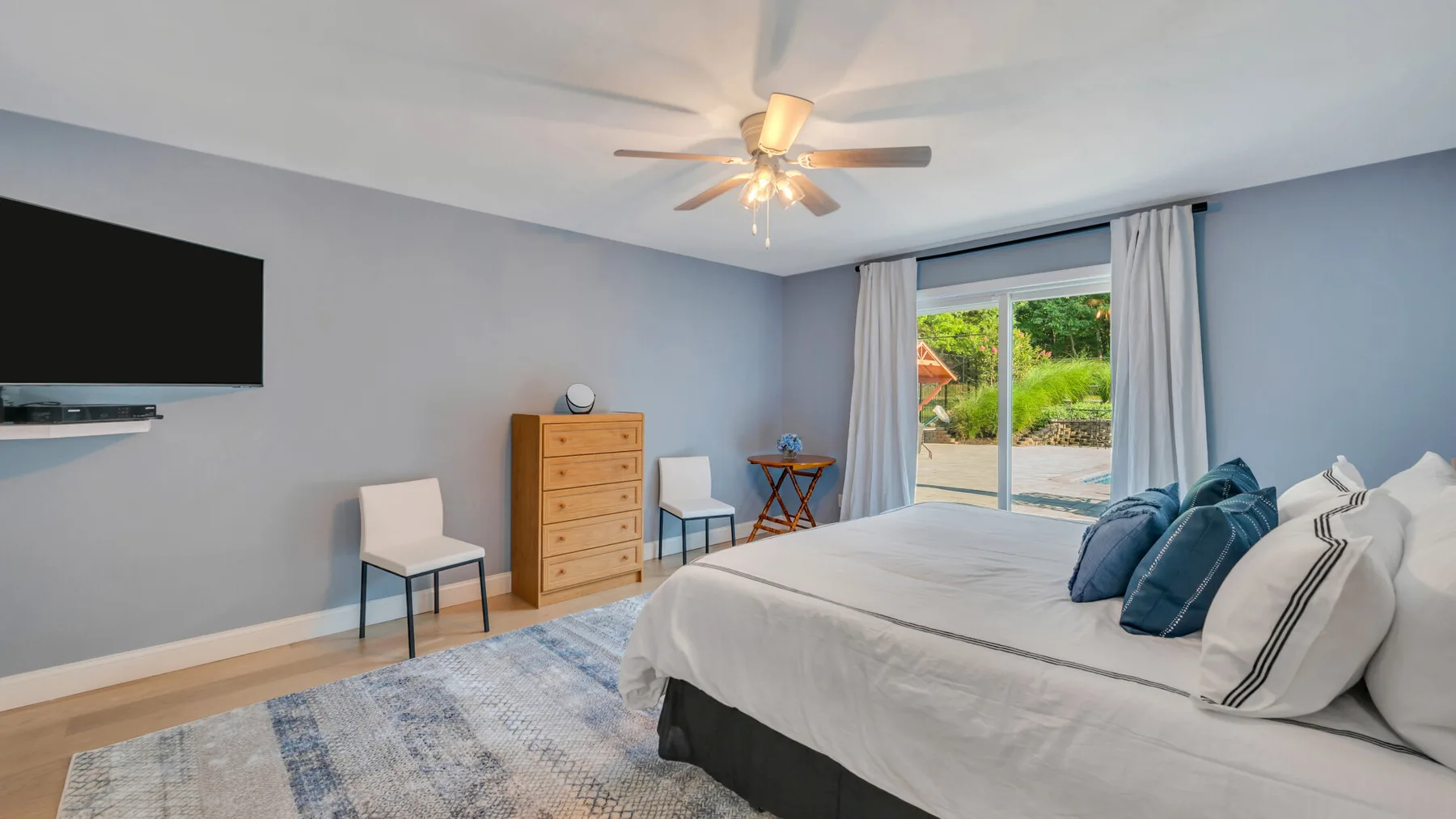 A bedroom with a large bed, a wall-mounted television, and a glass door opening to a patio.