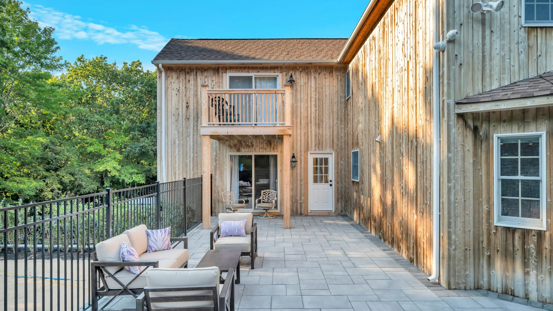 An outdoor patio beside a wood-sided building, with seating and a black railing.