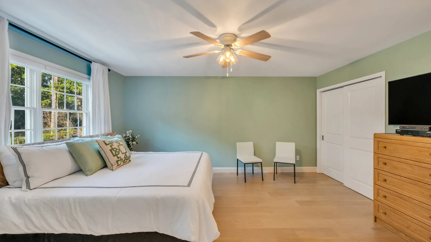 A bedroom with a bed beside a large window and a ceiling fan.