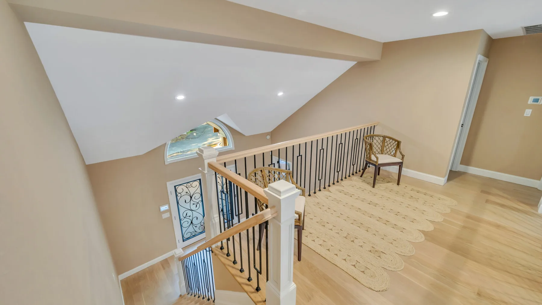 An upstairs landing with a staircase, decorative railing, and light wood flooring.
