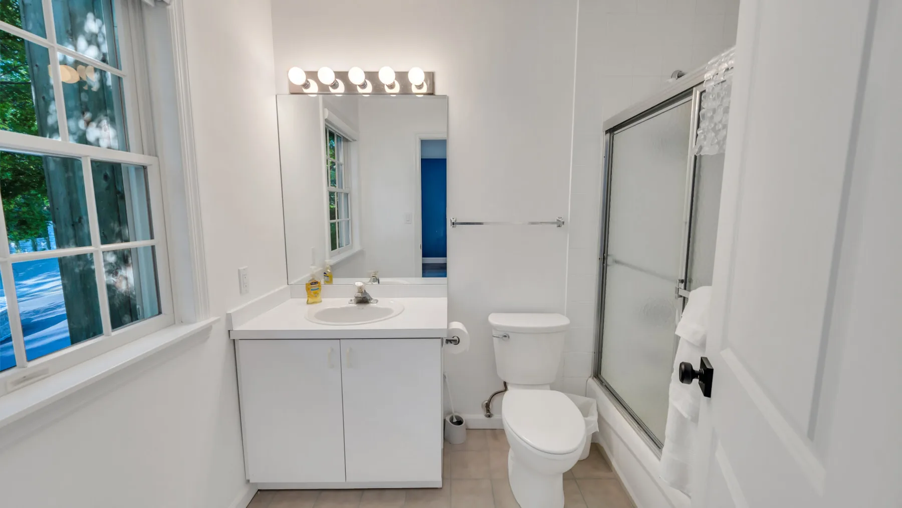 A bright bathroom with a vanity, mirror, toilet, and glass shower.