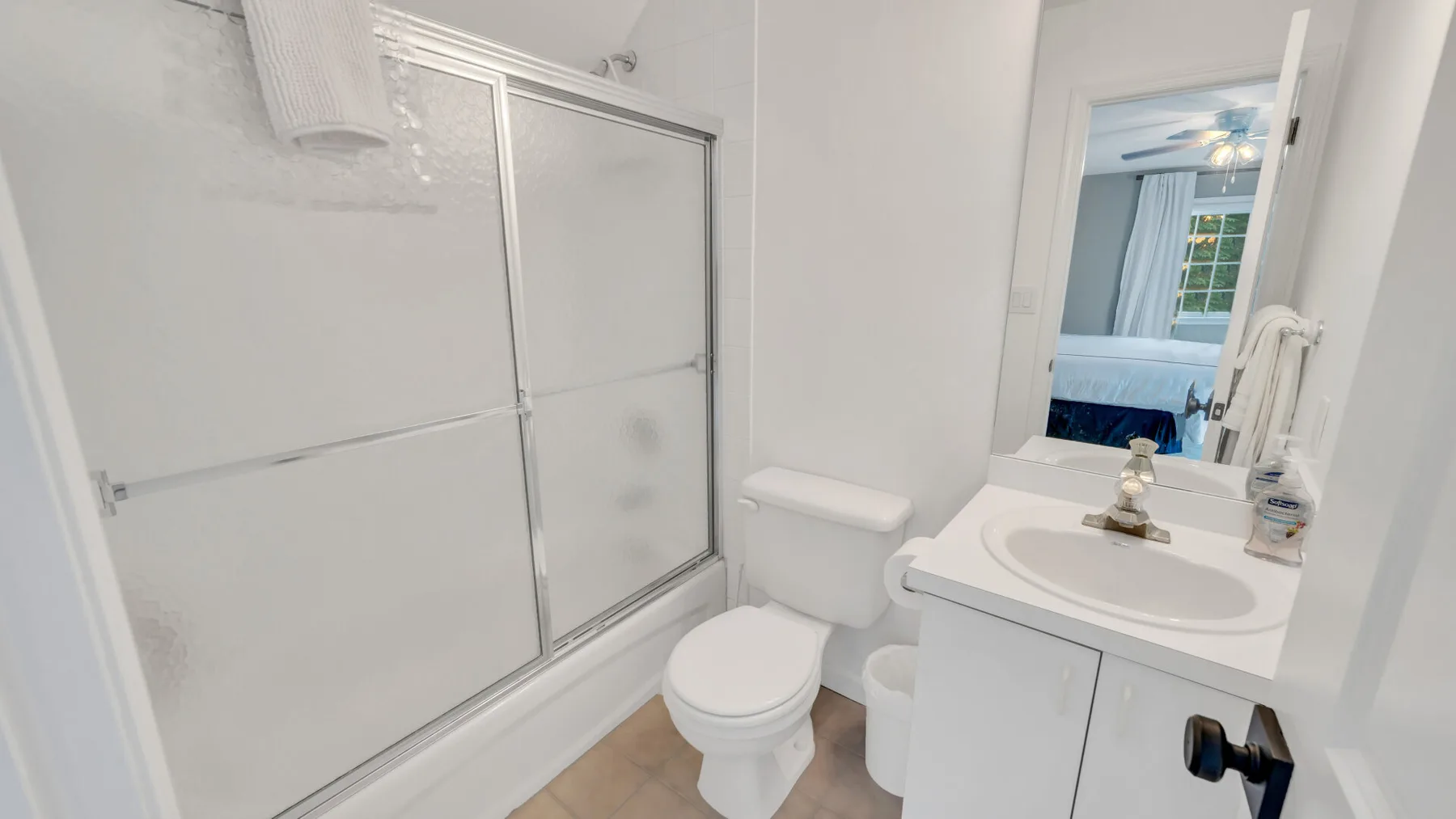 A bright bathroom with a shower, toilet, and sink beside a mirror.