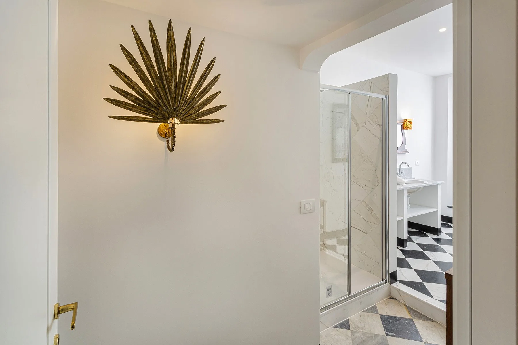 A doorway opens onto a bathroom with a glass shower and patterned floor.