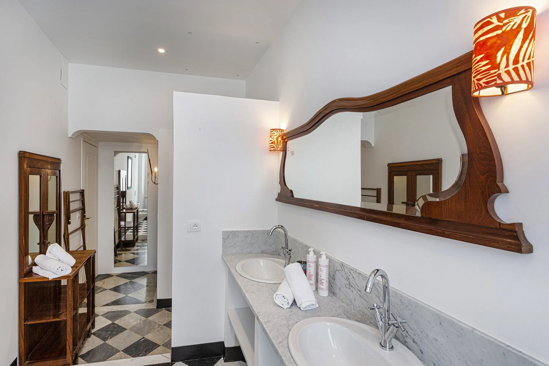 A bathroom vanity with two sinks, a large mirror, and a hallway beyond.
