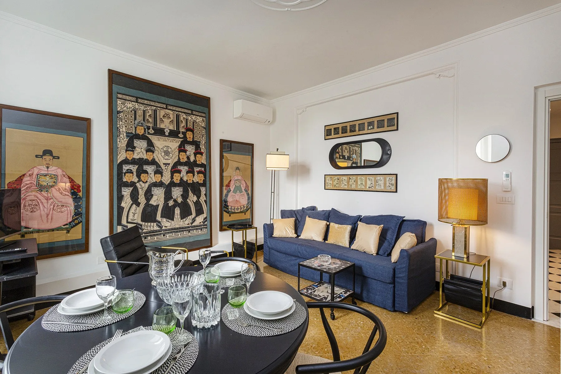 A living room with blue seating, framed artwork, and a dining table in the foreground.