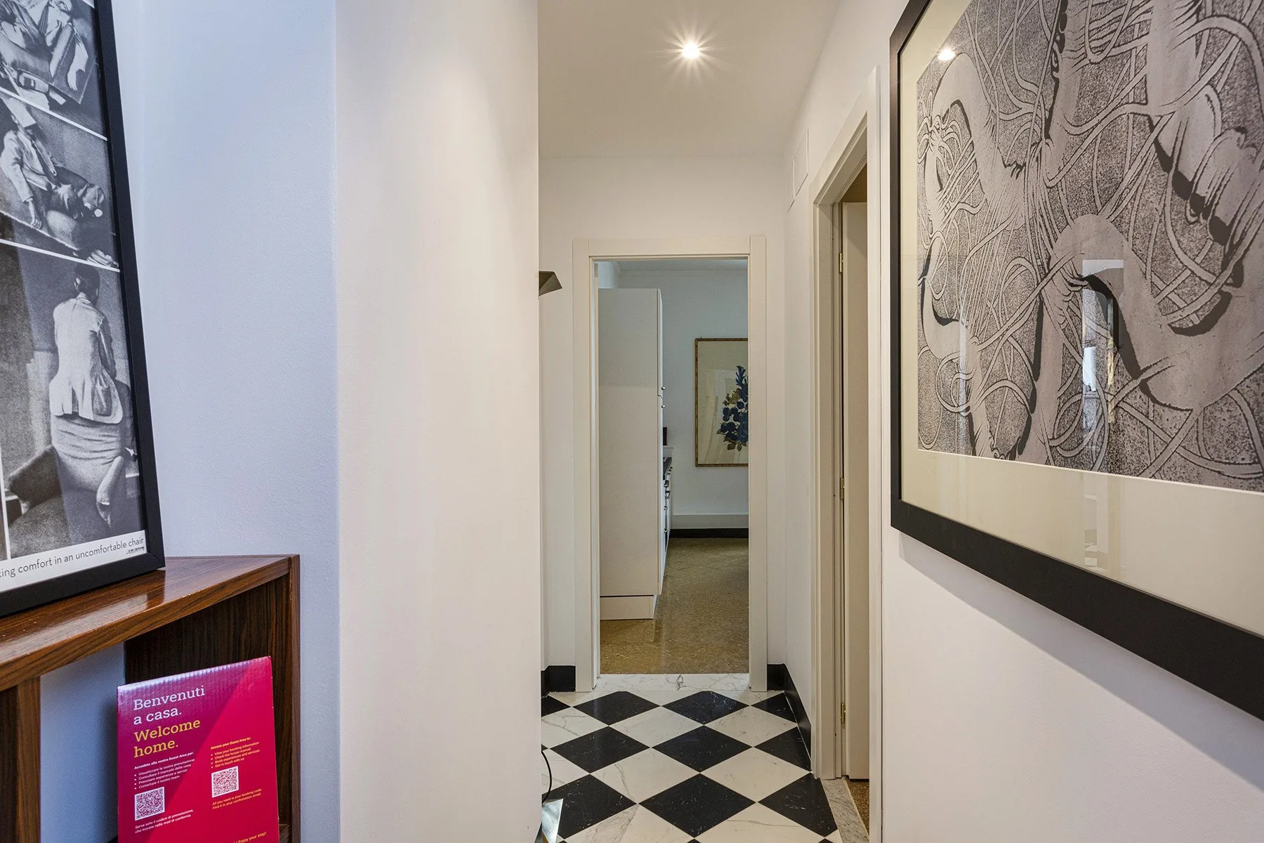 A narrow hallway with a black-and-white checkered floor and framed artwork.