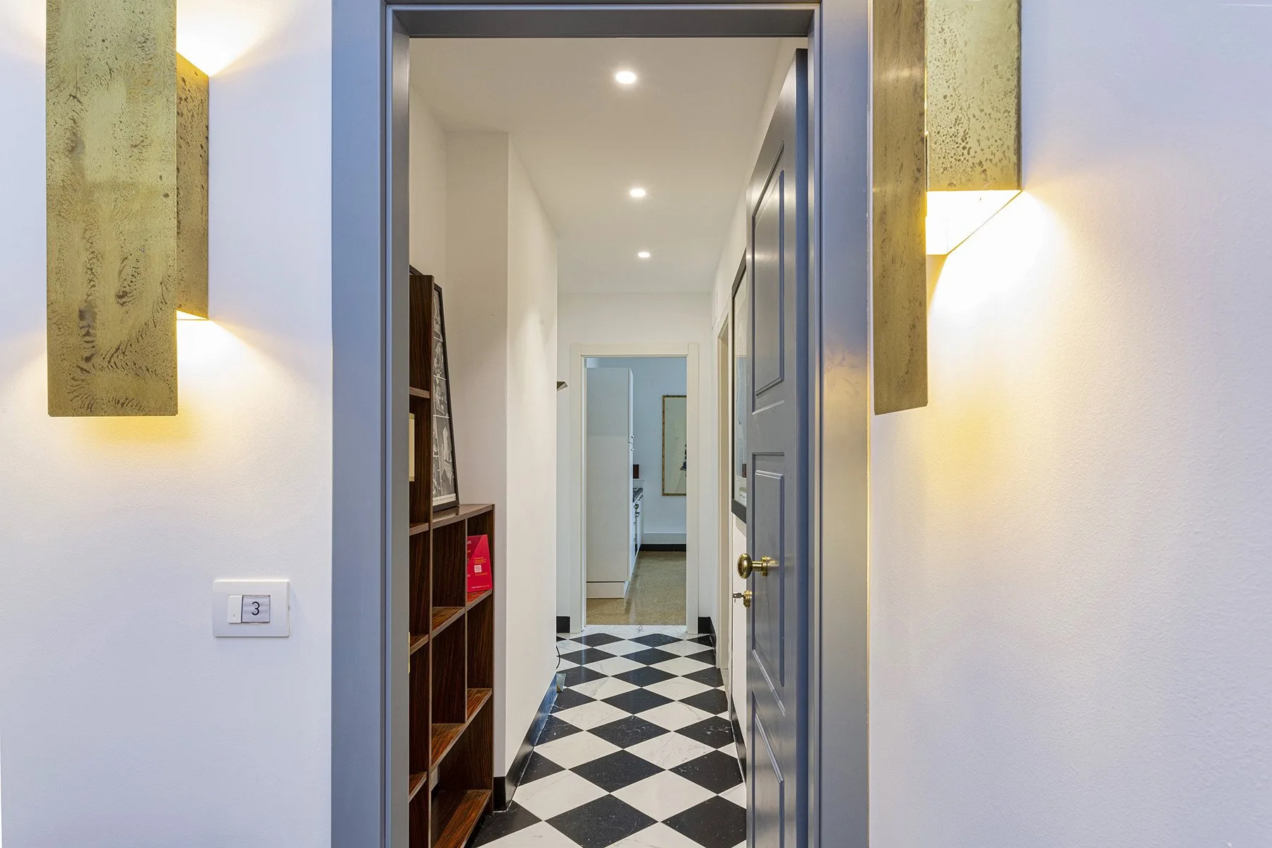 A hallway with a black-and-white checkered floor and recessed ceiling lights.