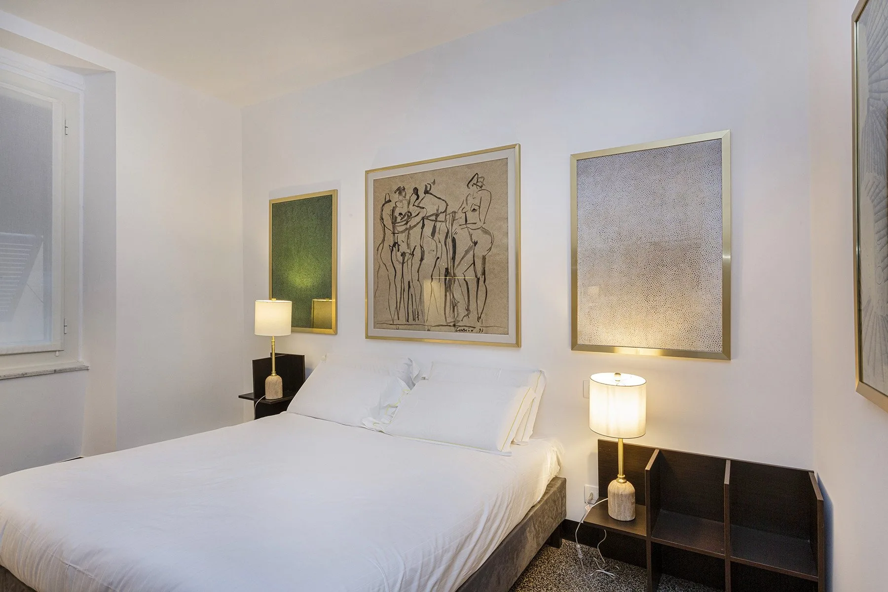 A bedroom with a neatly made bed, bedside lamps, and framed artwork.