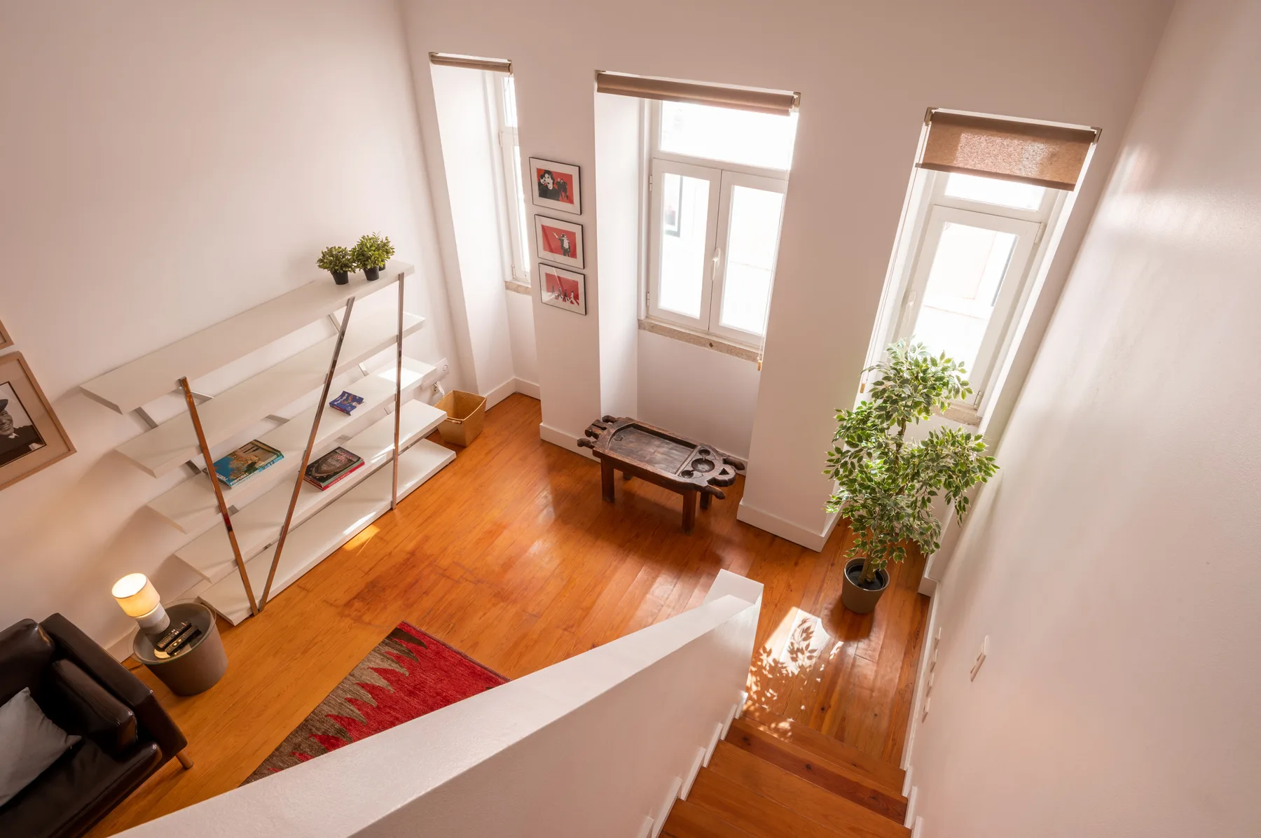A bright living room with tall windows, shelving, and a small table.