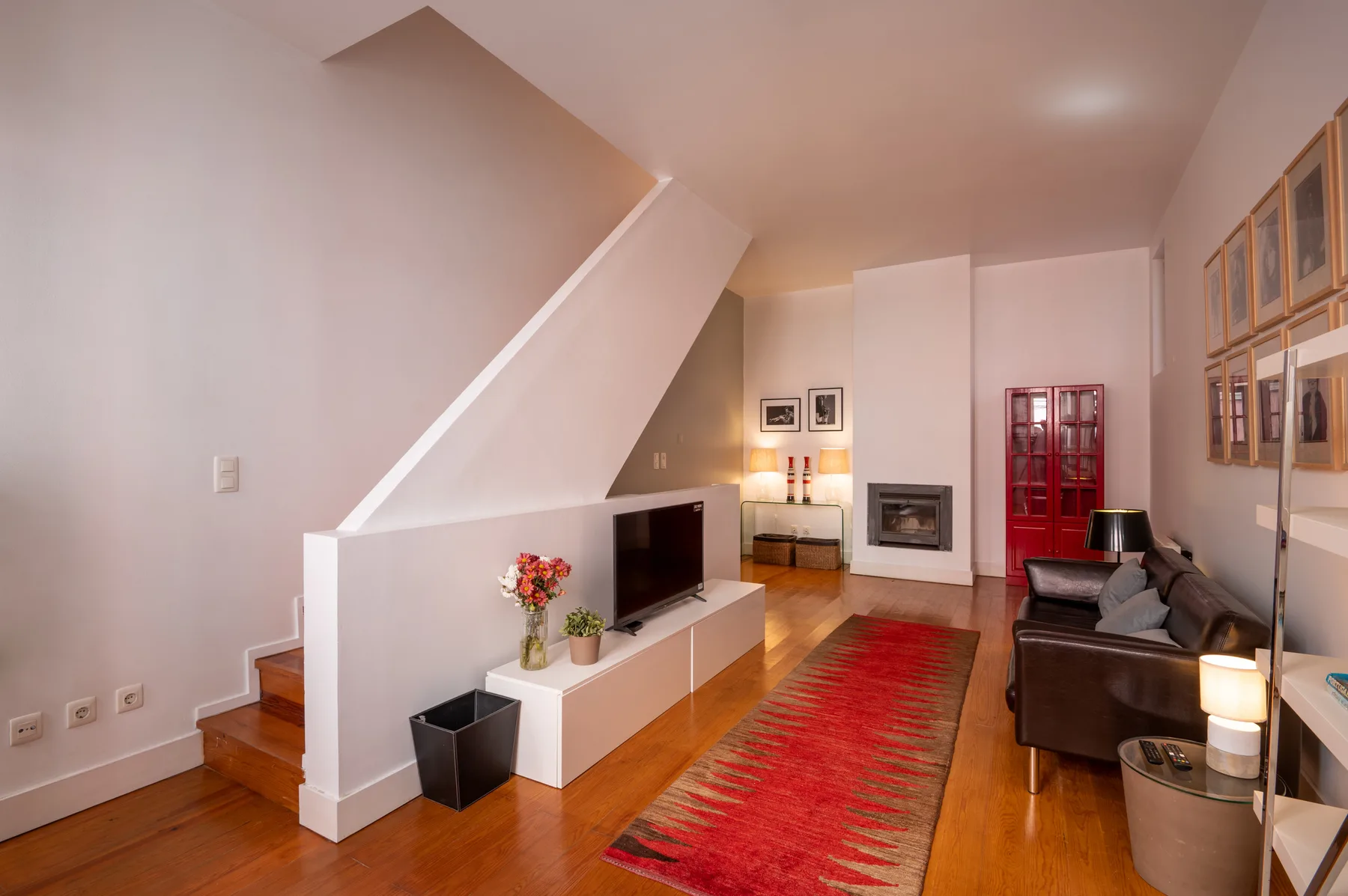 A living room with a television, seating, and a red rug beneath the staircase.
