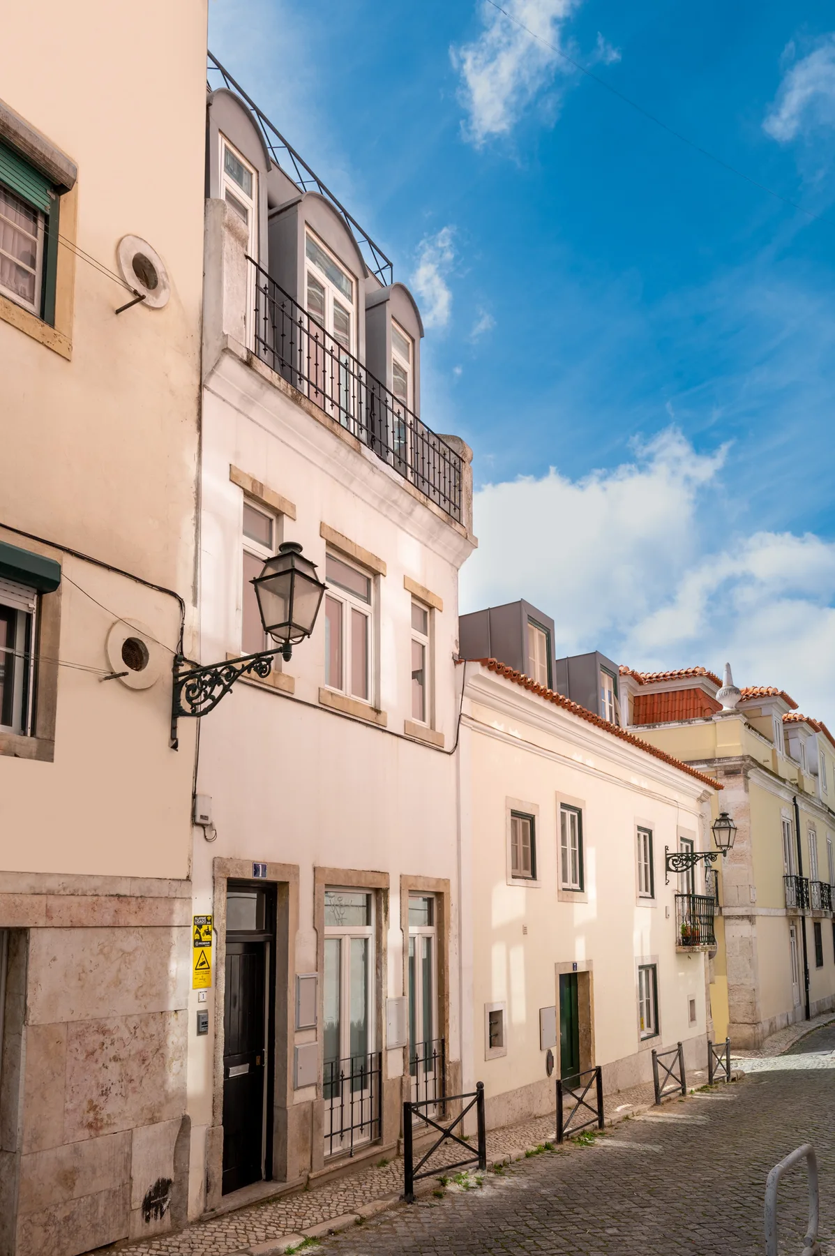 Street scene with closely spaced buildings and cobblestone paving under a blue sky.