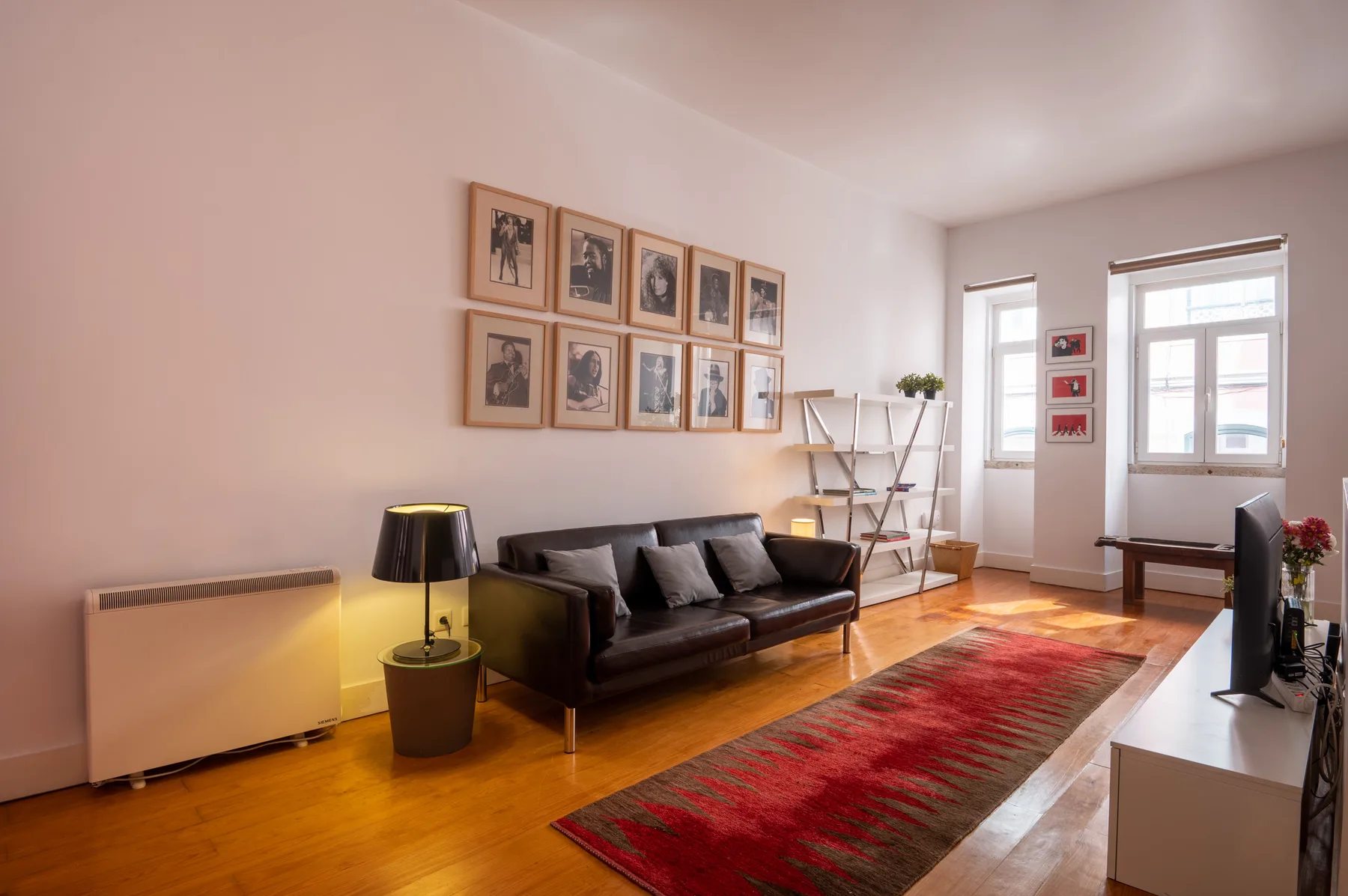 A living room with dark seating, framed pictures, and a red rug.