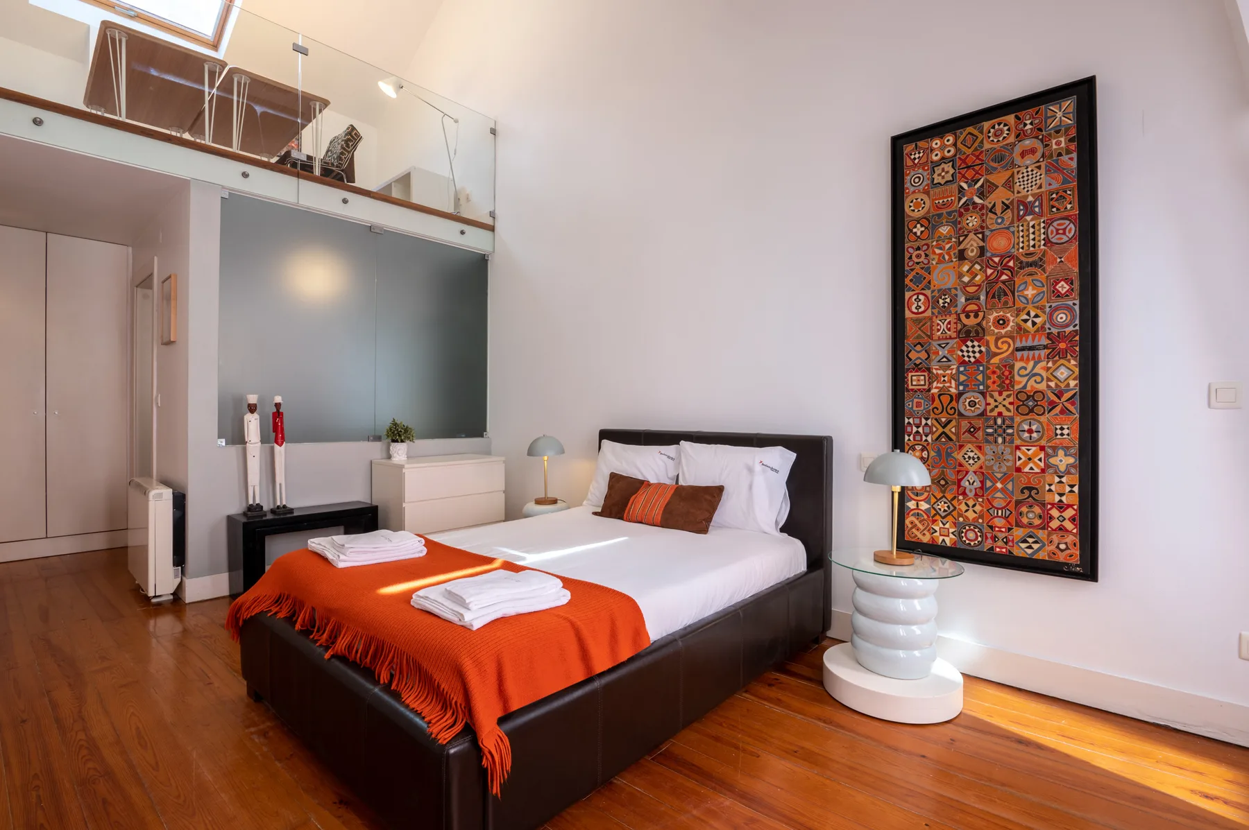 A bedroom with a double bed, orange bedding, and colorful wall art.