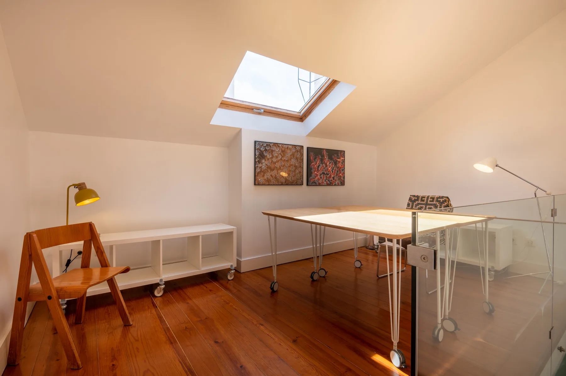 A bright attic workspace with a skylight, desk, and wooden flooring.