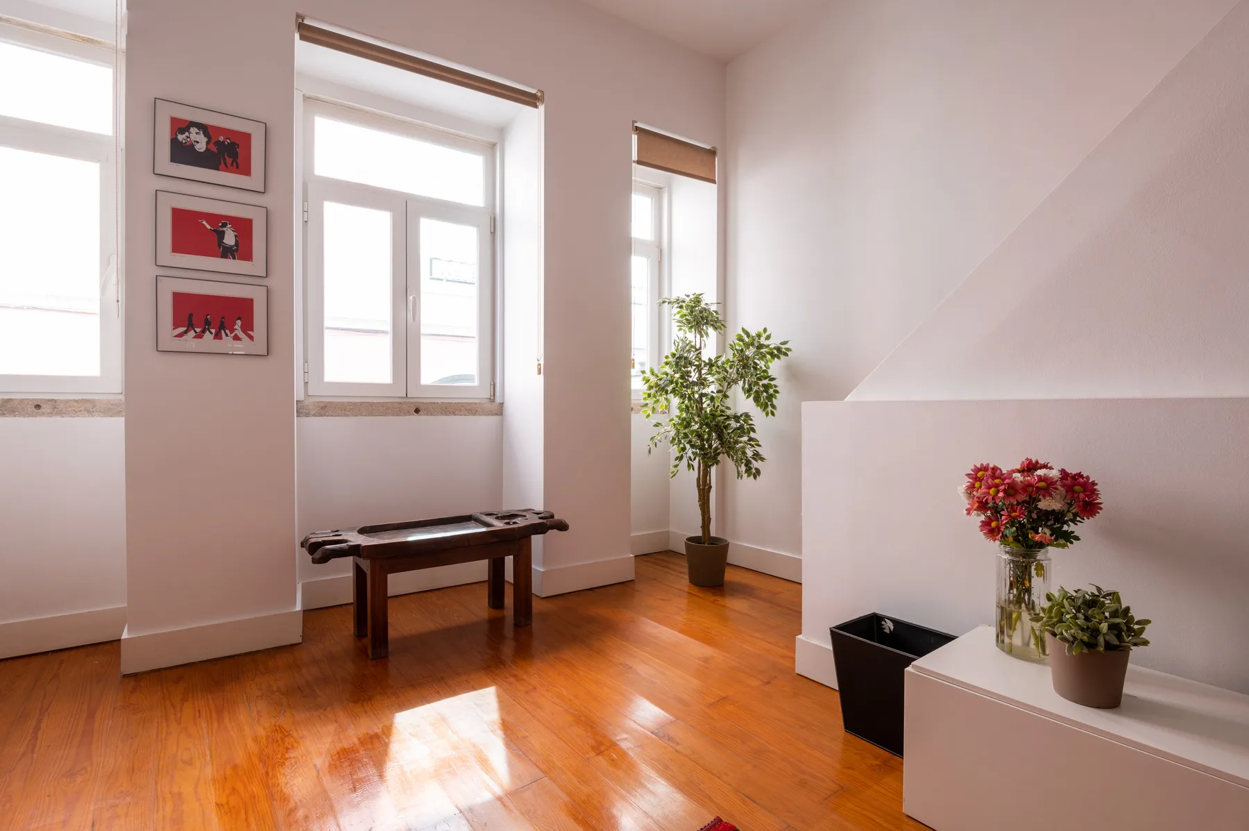 A bright room with tall windows, polished wood flooring, and a small table.