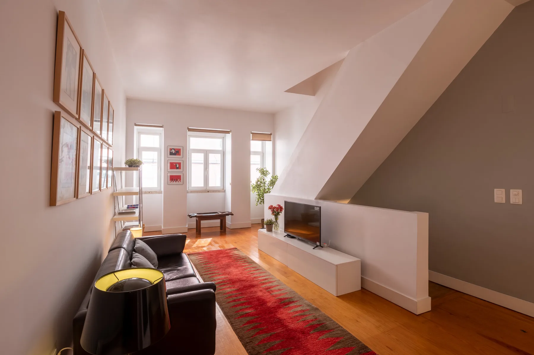 A bright living room with seating, a television, and a red patterned rug.