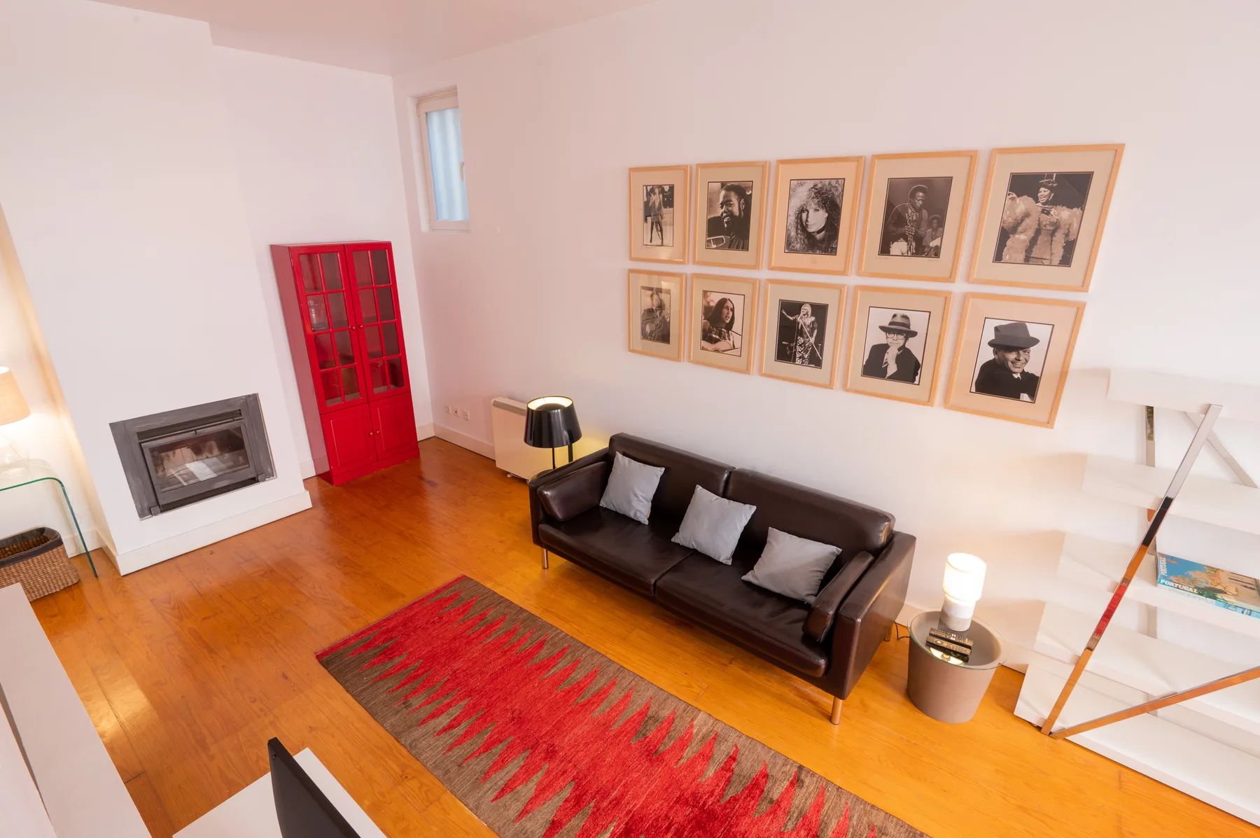 A living room with dark seating, framed portraits, and a red door.