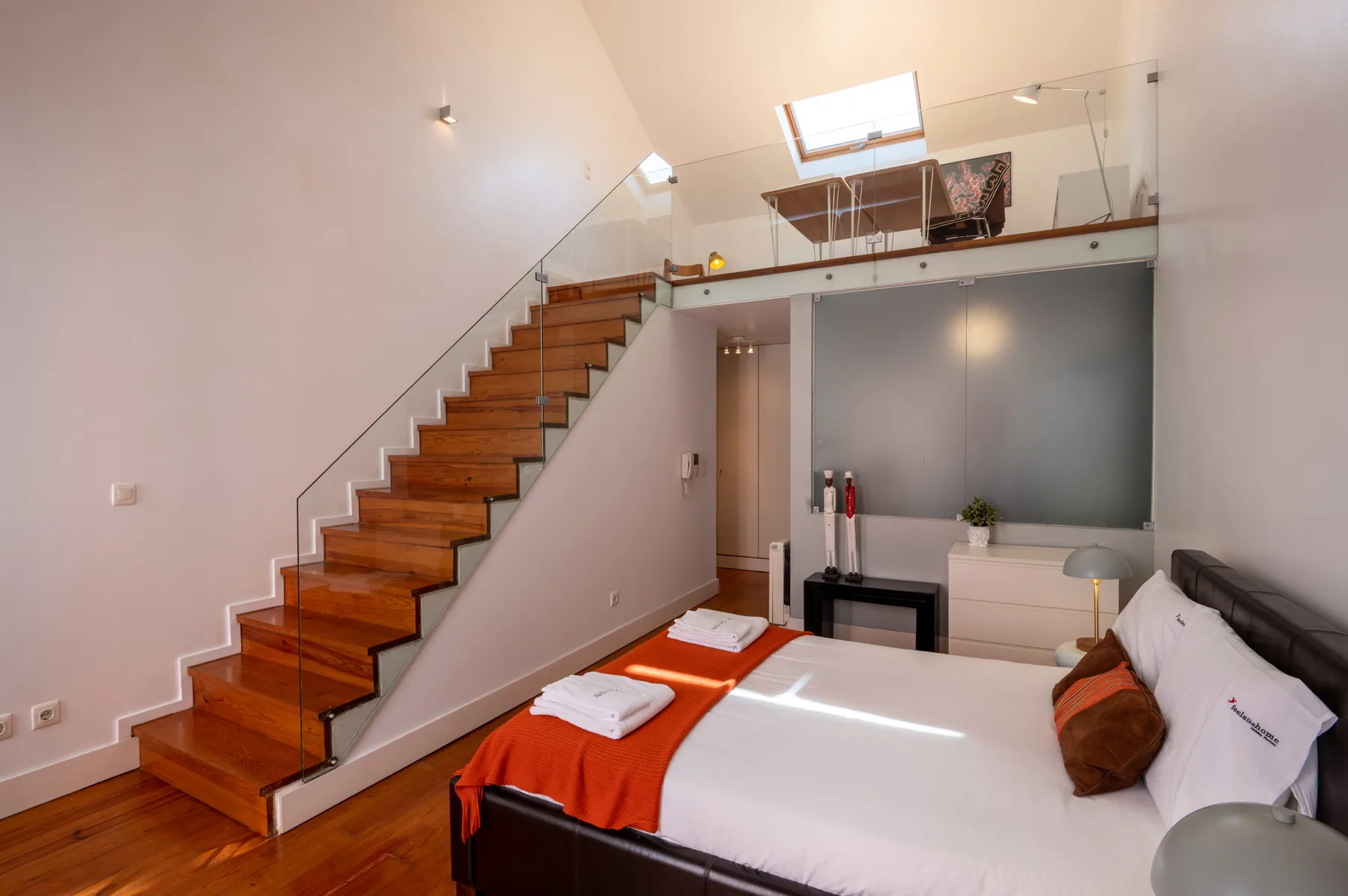 A bedroom with a bed, wooden staircase, and loft seating area.