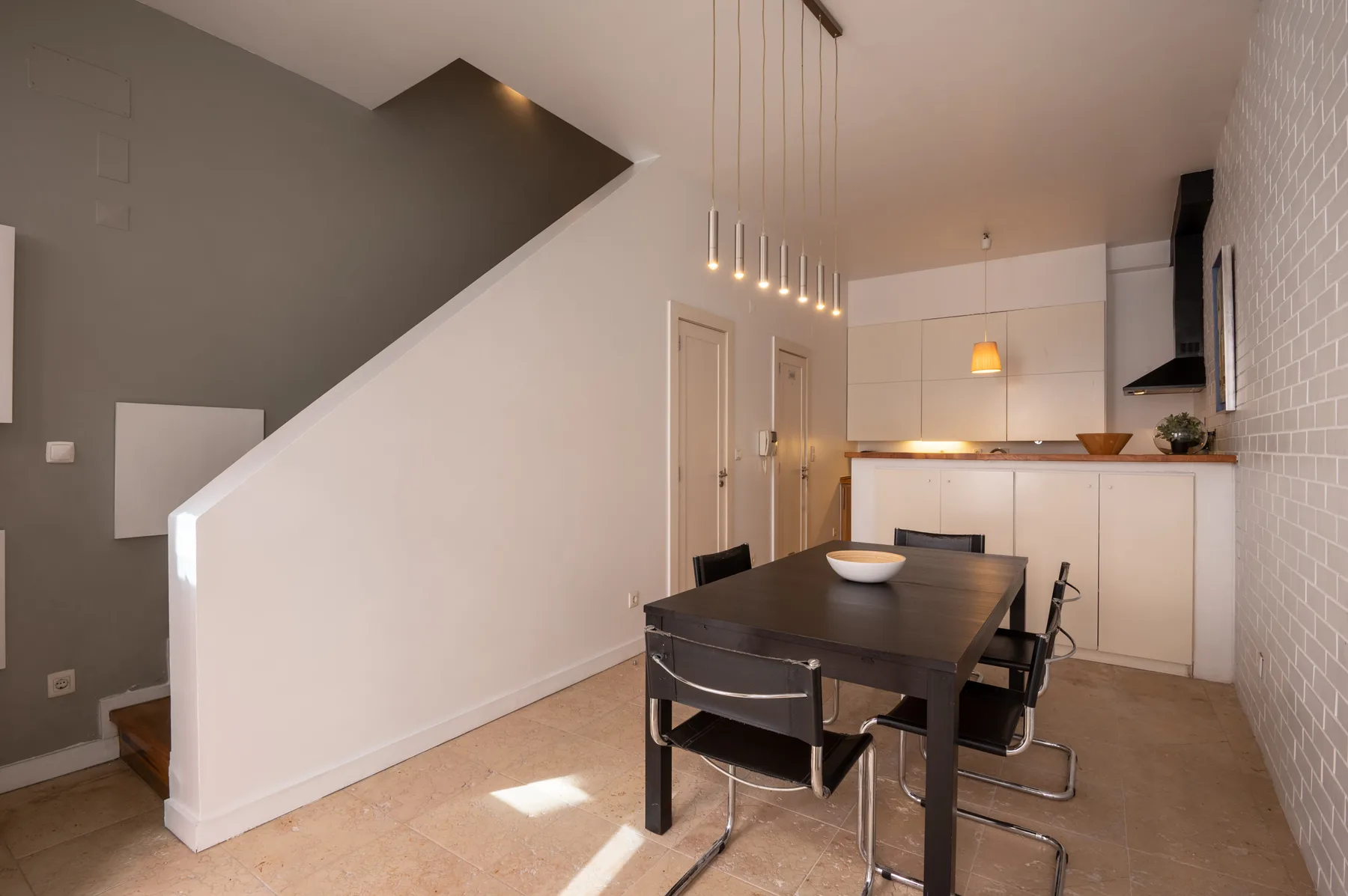 Dining area with a dark table and pendant lights beside a compact kitchen.