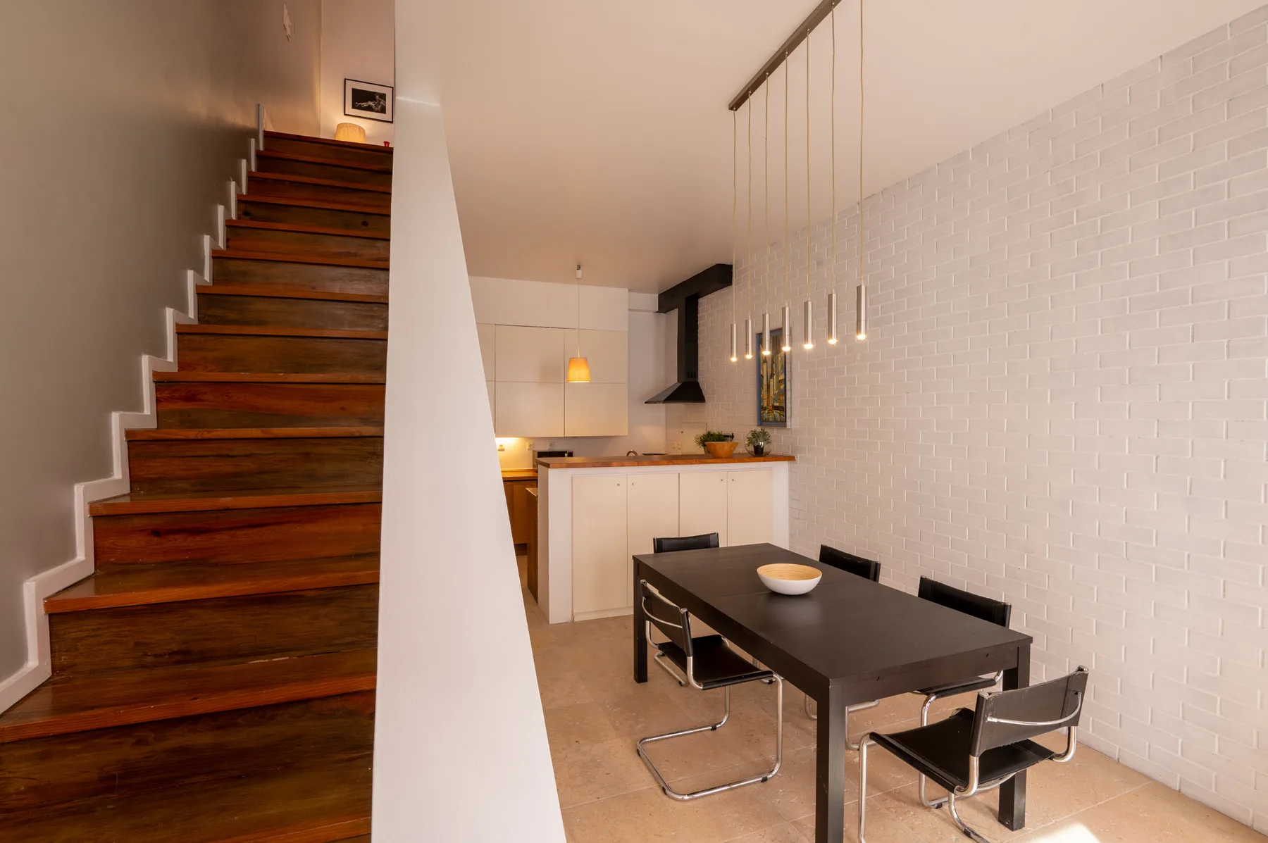 A dining area with a dark table beside a compact kitchen and staircase.