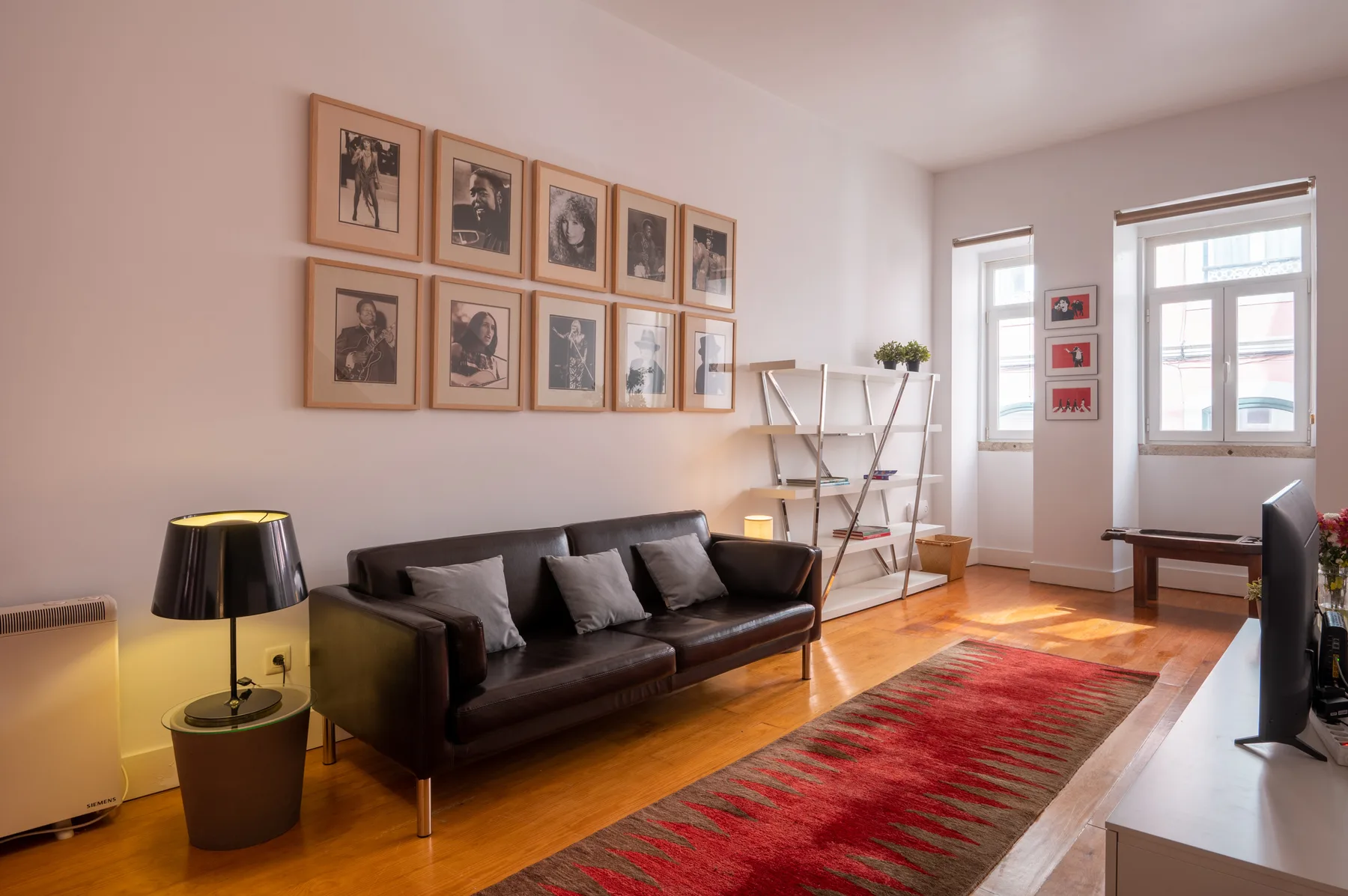 A bright living room with dark seating, framed artwork, and a red rug.