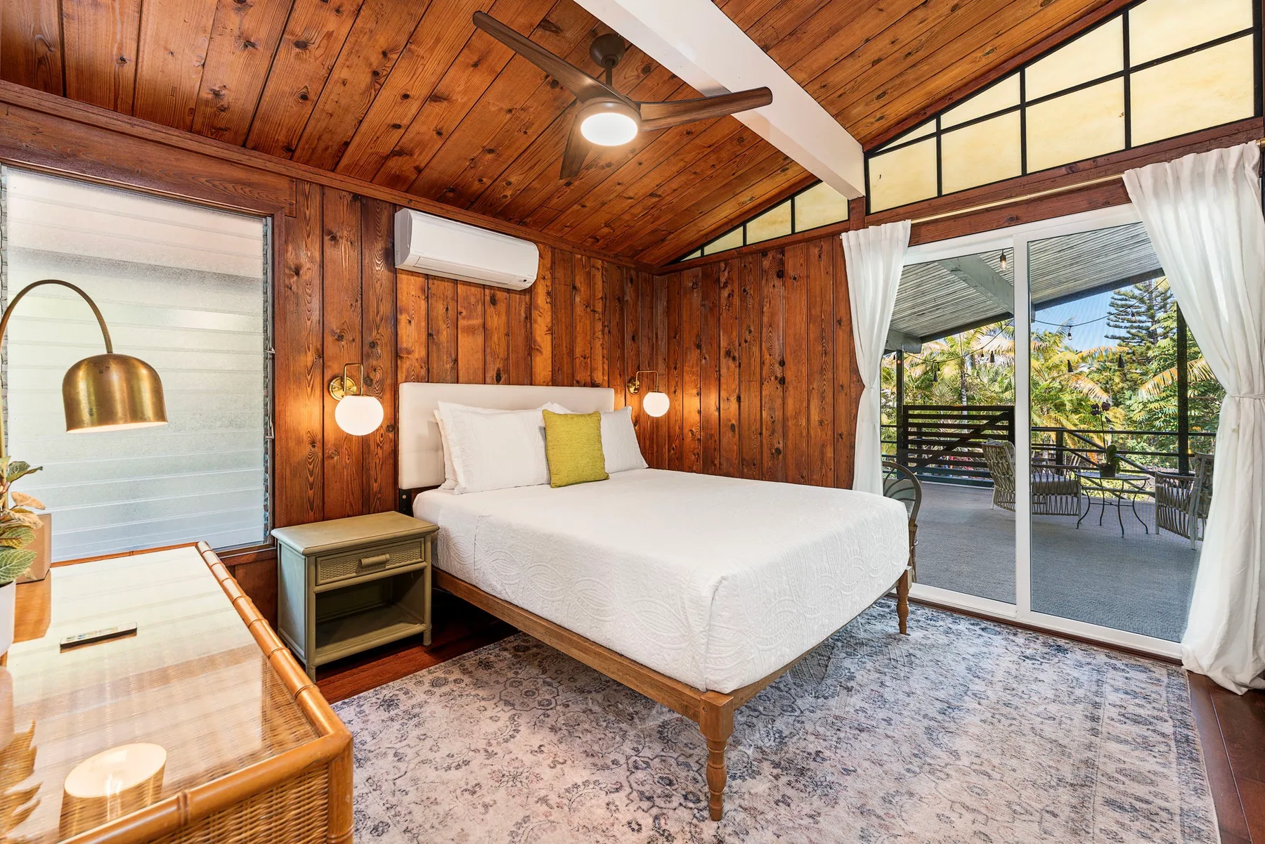 A bedroom with a bed, wood-paneled walls, and glass doors opening onto a patio.