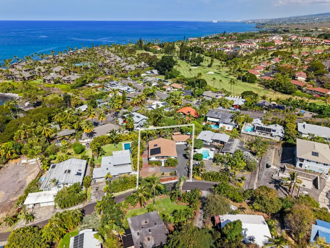 Aerial view of a coastal residential neighborhood with green fields and ocean.