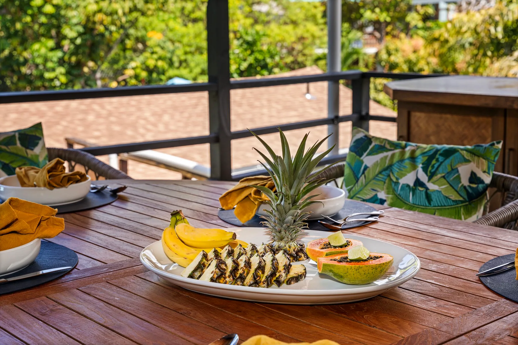An outdoor dining table holds a platter of fruit beside cushioned seating.