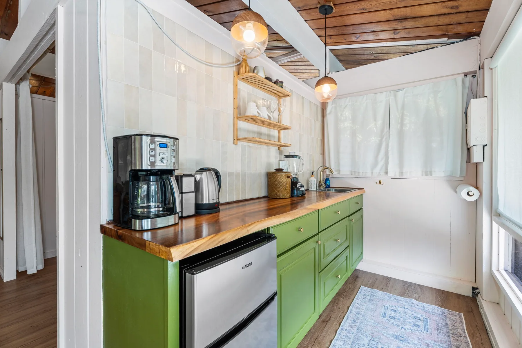 A compact kitchen with green cabinets, a wooden countertop, and a coffee maker.