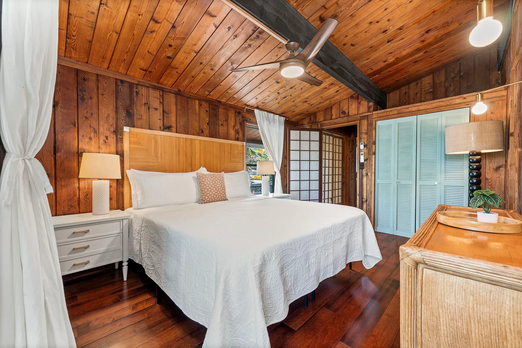 A bedroom with a large bed, wood-paneled walls, and a sloped wooden ceiling.